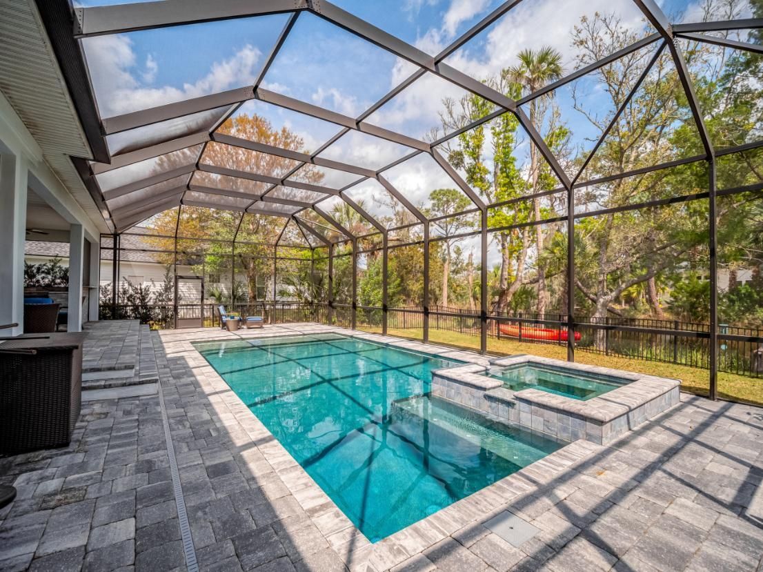 Screened-in patio with turquoise pool, spa, and stone decking beside a house