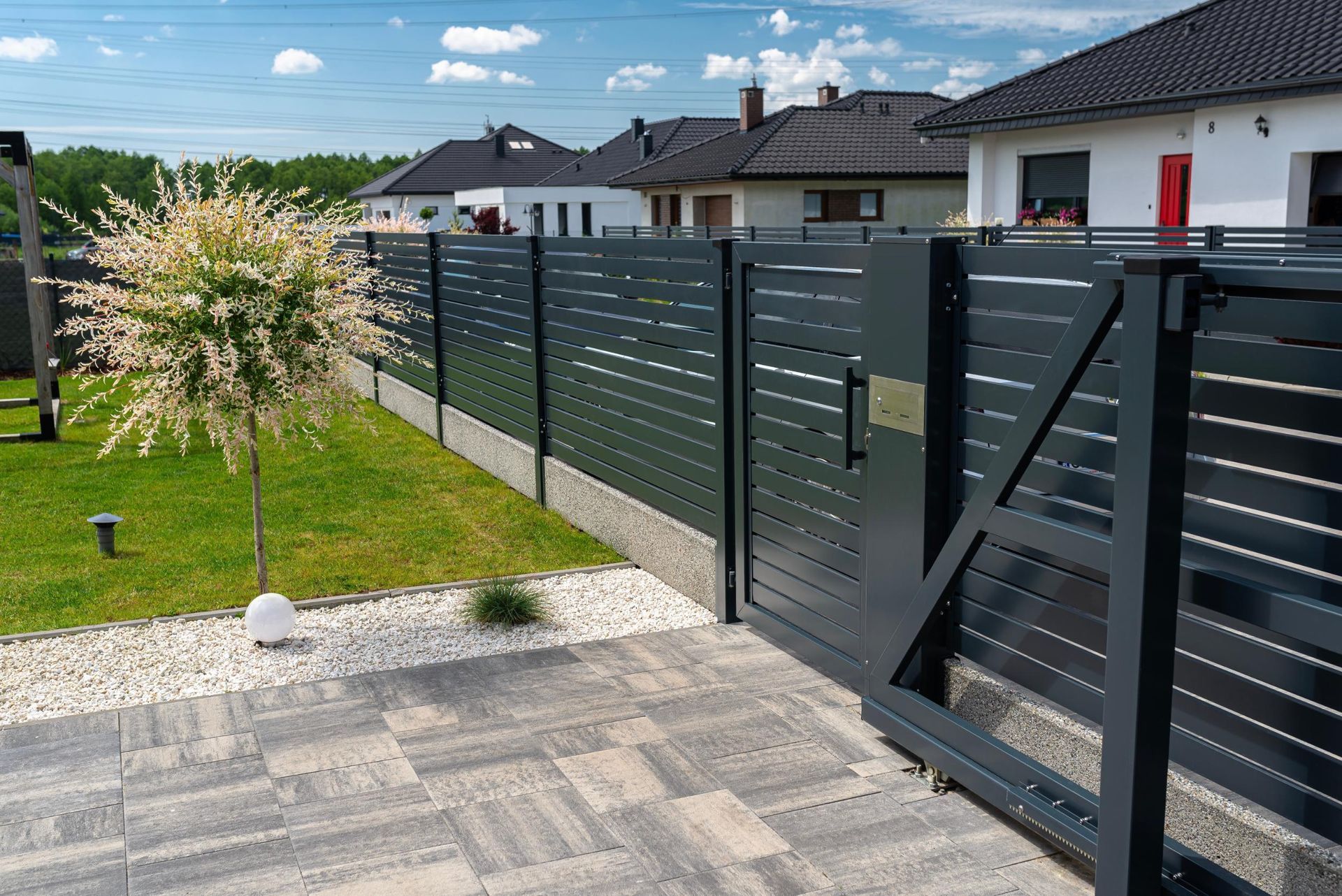 Modern black metal fence with gate beside a lawn and paved patio in a suburban yard