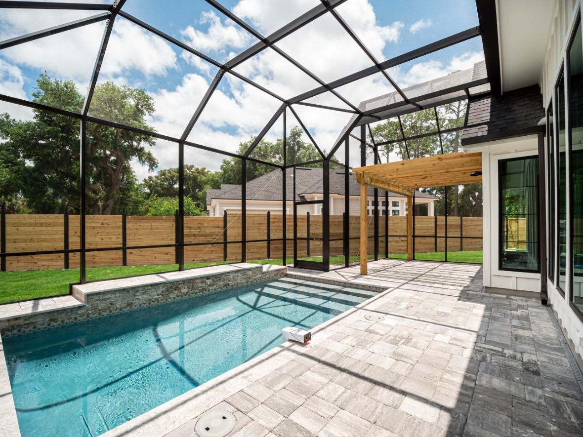 Screened backyard patio with a swimming pool, pavers, and covered seating area under a glass enclosure