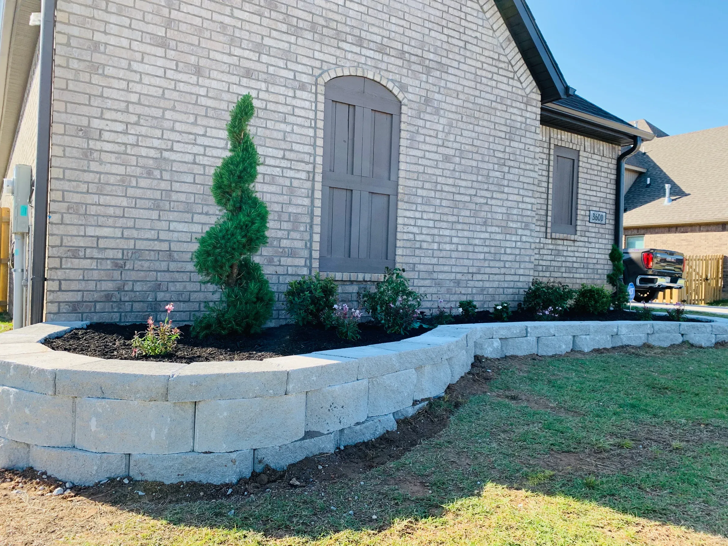 Gray brick house with a curved retaining wall, lawn, and landscaped flower bed.