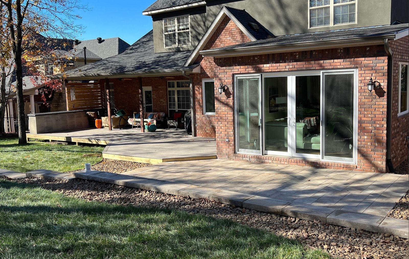 Backyard patio with brick building, stone path, and grassy yard on a sunny day.
