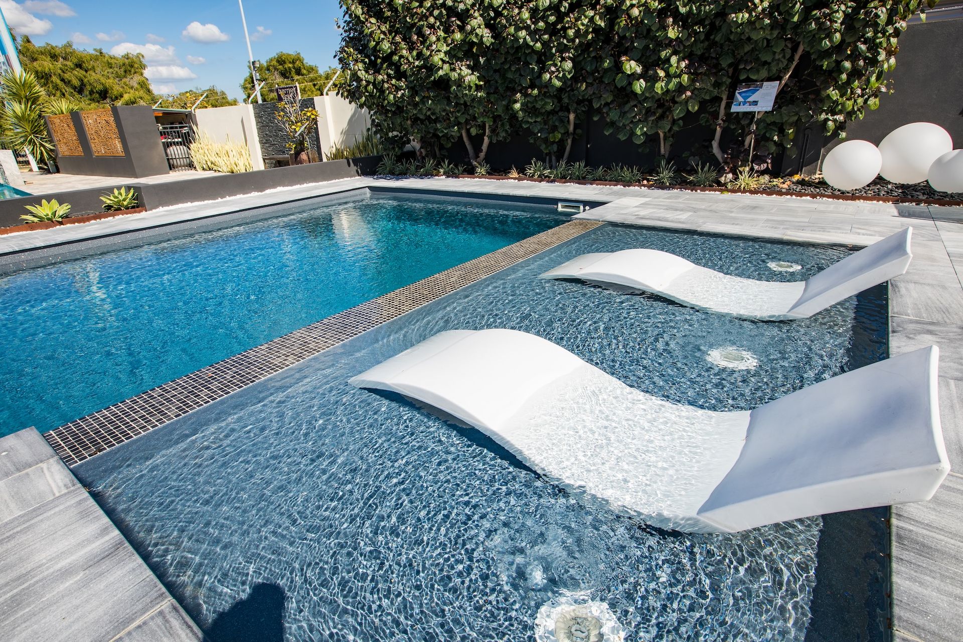Pool with white lounge chairs, blue water, stone patio, and surrounding greenery.