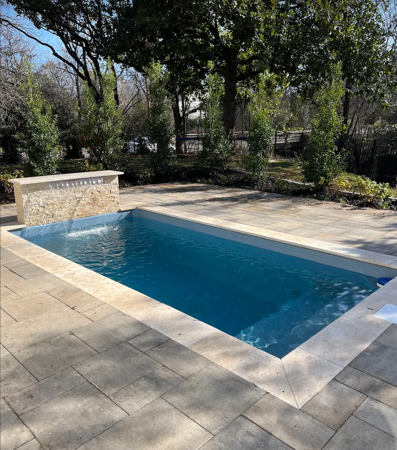 Rectangular pool with blue water and stone surround, near a stone feature, surrounded by trees.