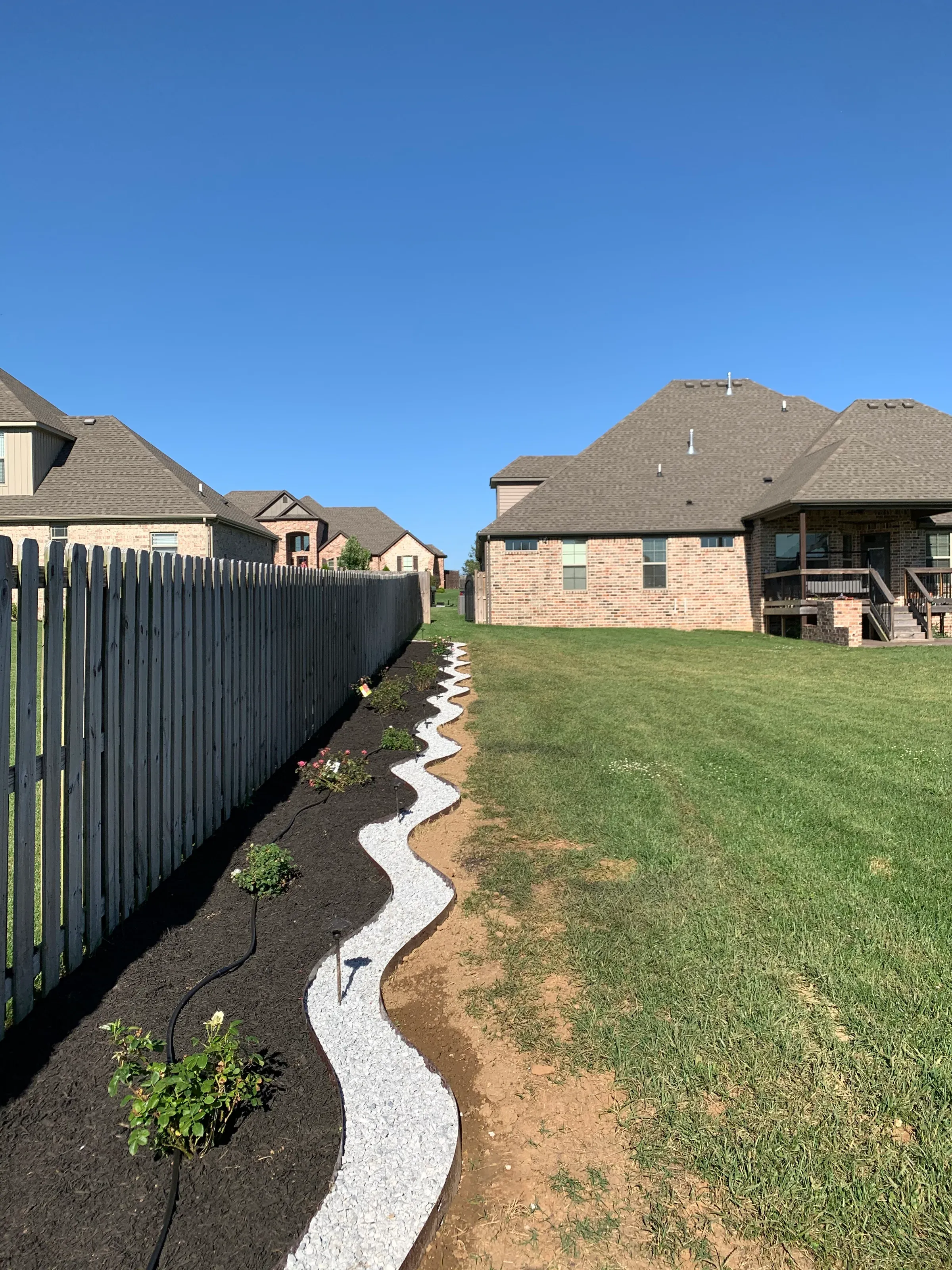 Backyard landscaping with a wavy gravel path, mulch, grass, and a wooden fence.
