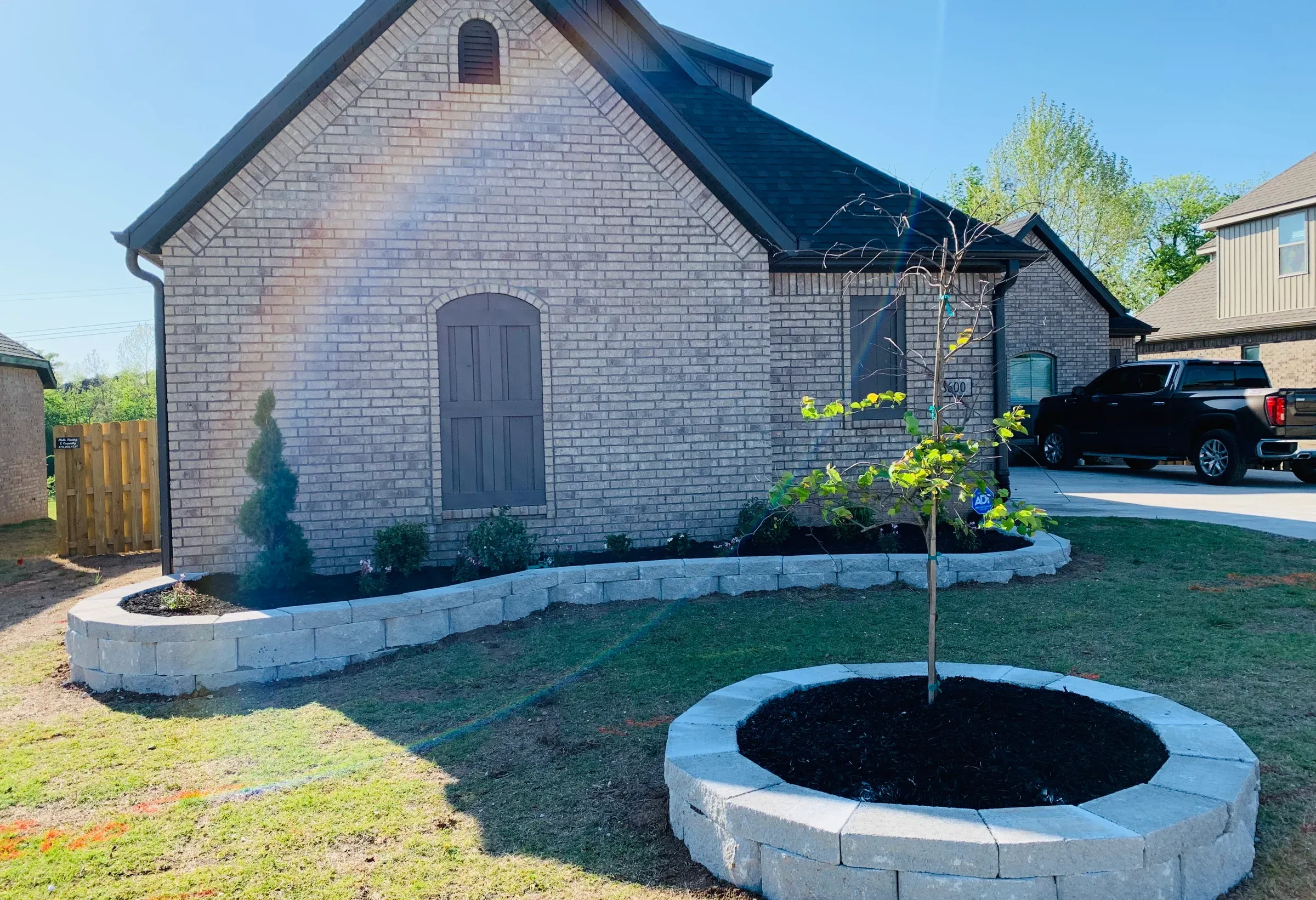 House with stone facade and landscaped yard with retaining walls and a tree.