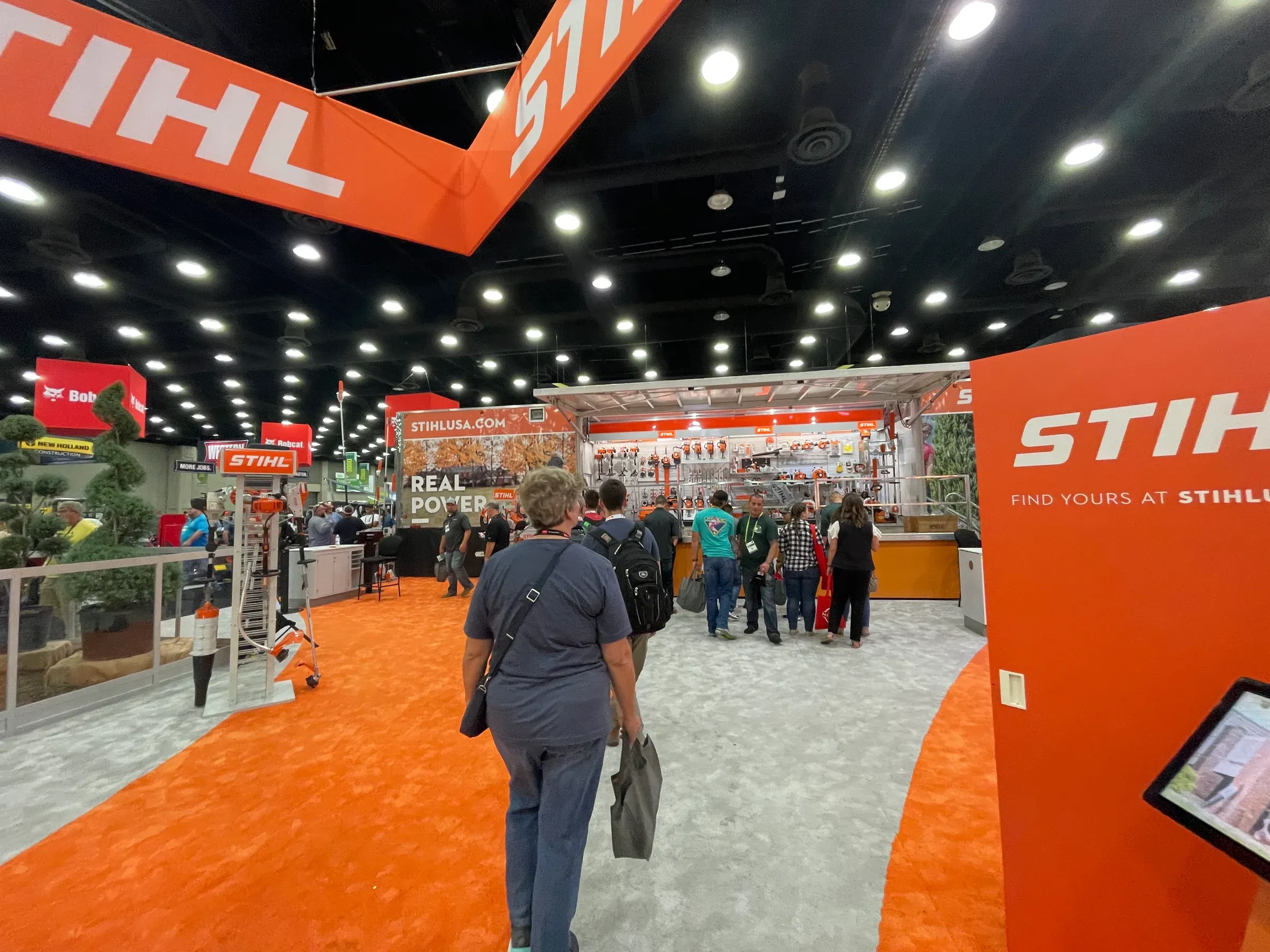 People at a trade show with orange and white Stihl displays.