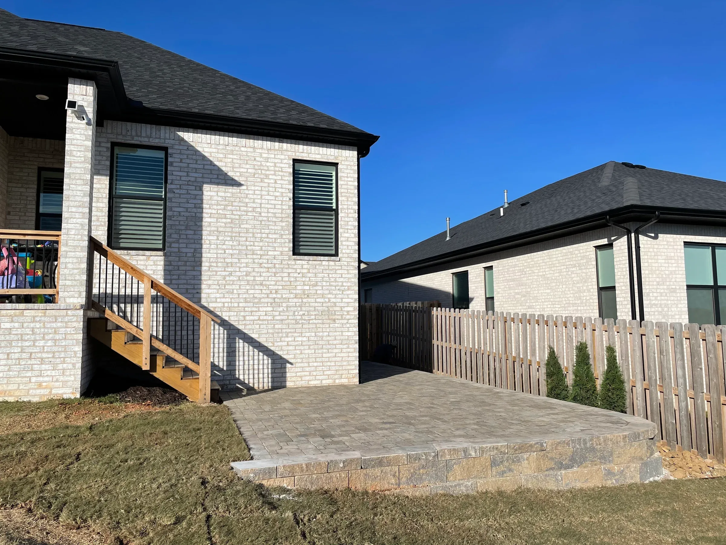 Brick house with a patio and wooden stairs leading to a backyard with a fence.