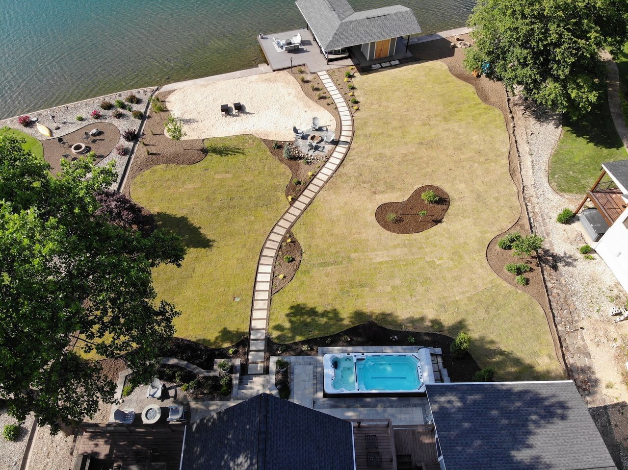 Aerial view of a landscaped yard with a pool, stone path, dock, and lake.