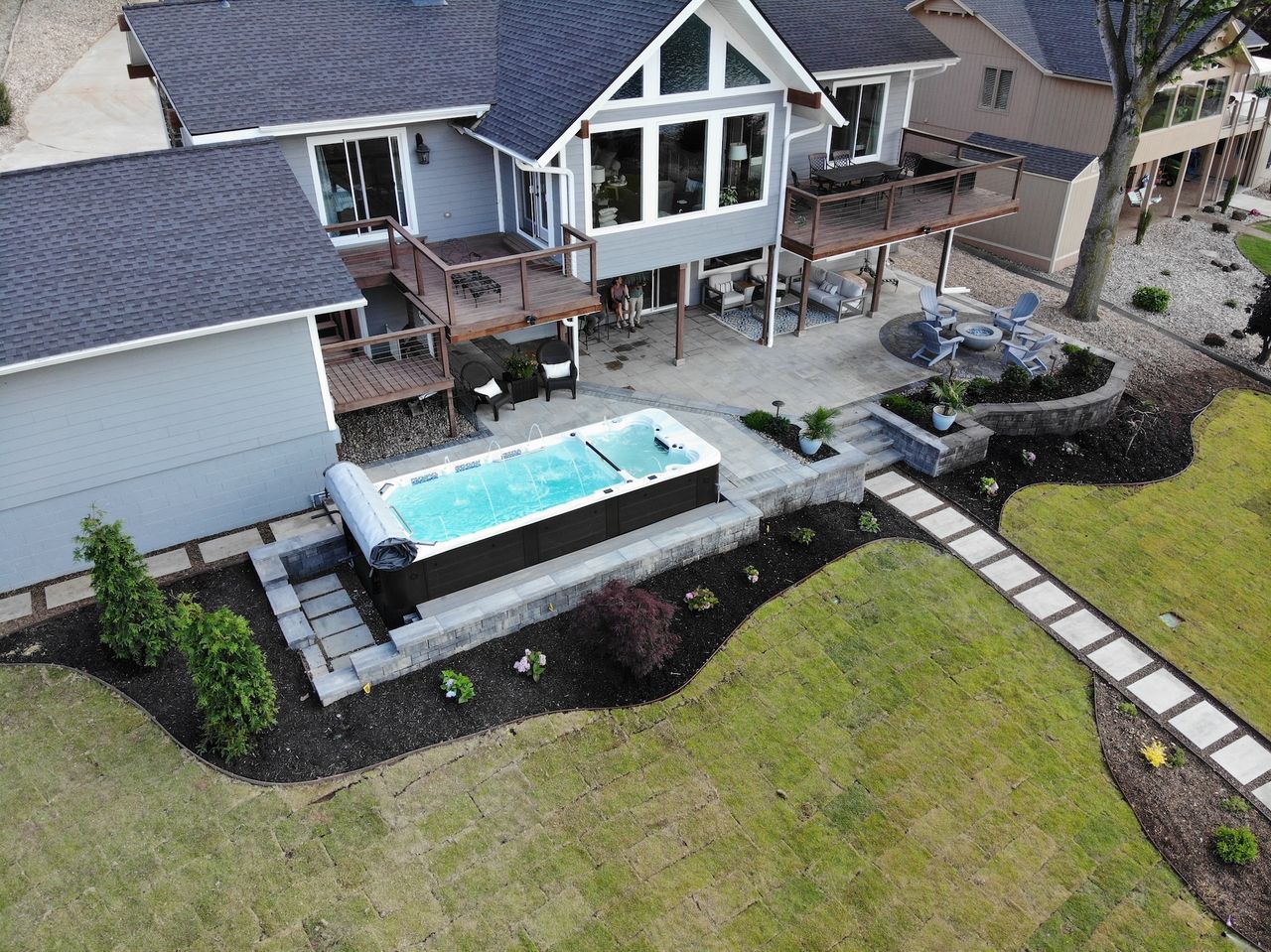 Aerial view of a home with a small, rectangular pool on a stone patio surrounded by landscaping and a lawn.