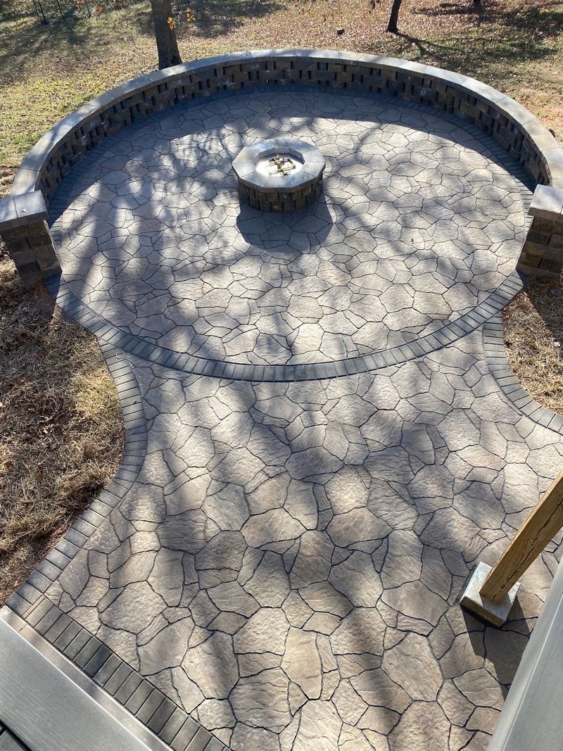 Stone patio with built-in fire pit and curved seating wall, outdoors with tree shadows.