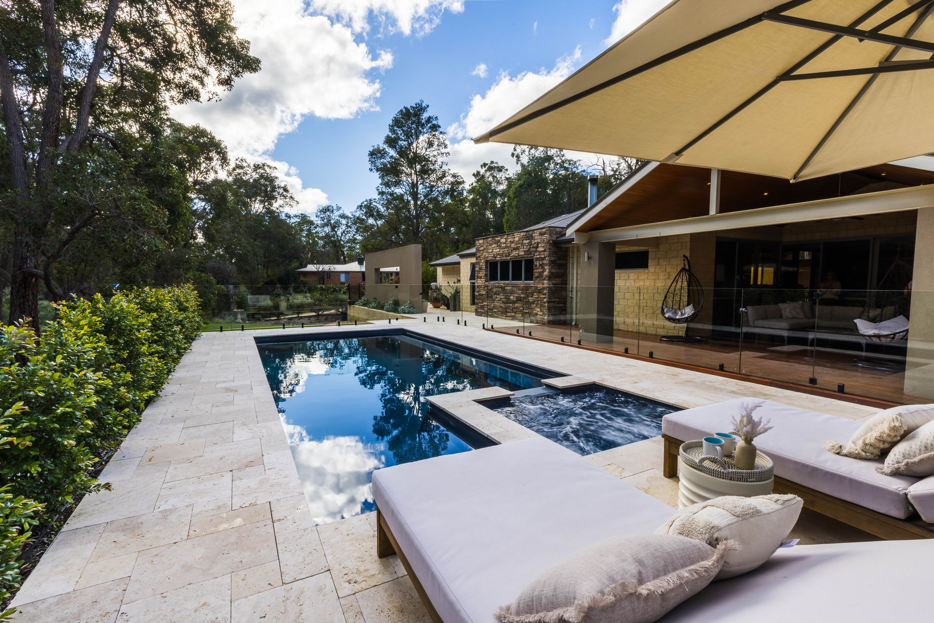 Swimming pool and lounge chairs on a patio beside a house; umbrella provides shade.