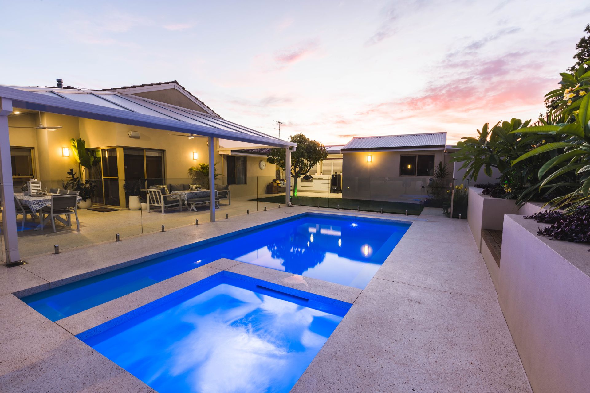 Backyard pool and spa area at dusk with a home, patio, and landscaped beds.