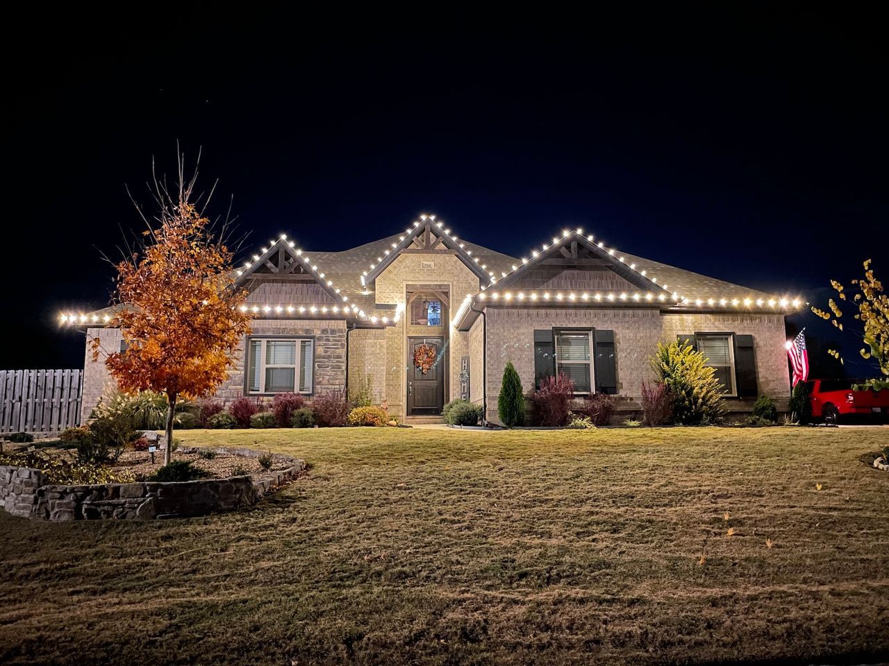 House with white Christmas lights on the roof, lit up at night. Brown brick exterior with a dry lawn in front.