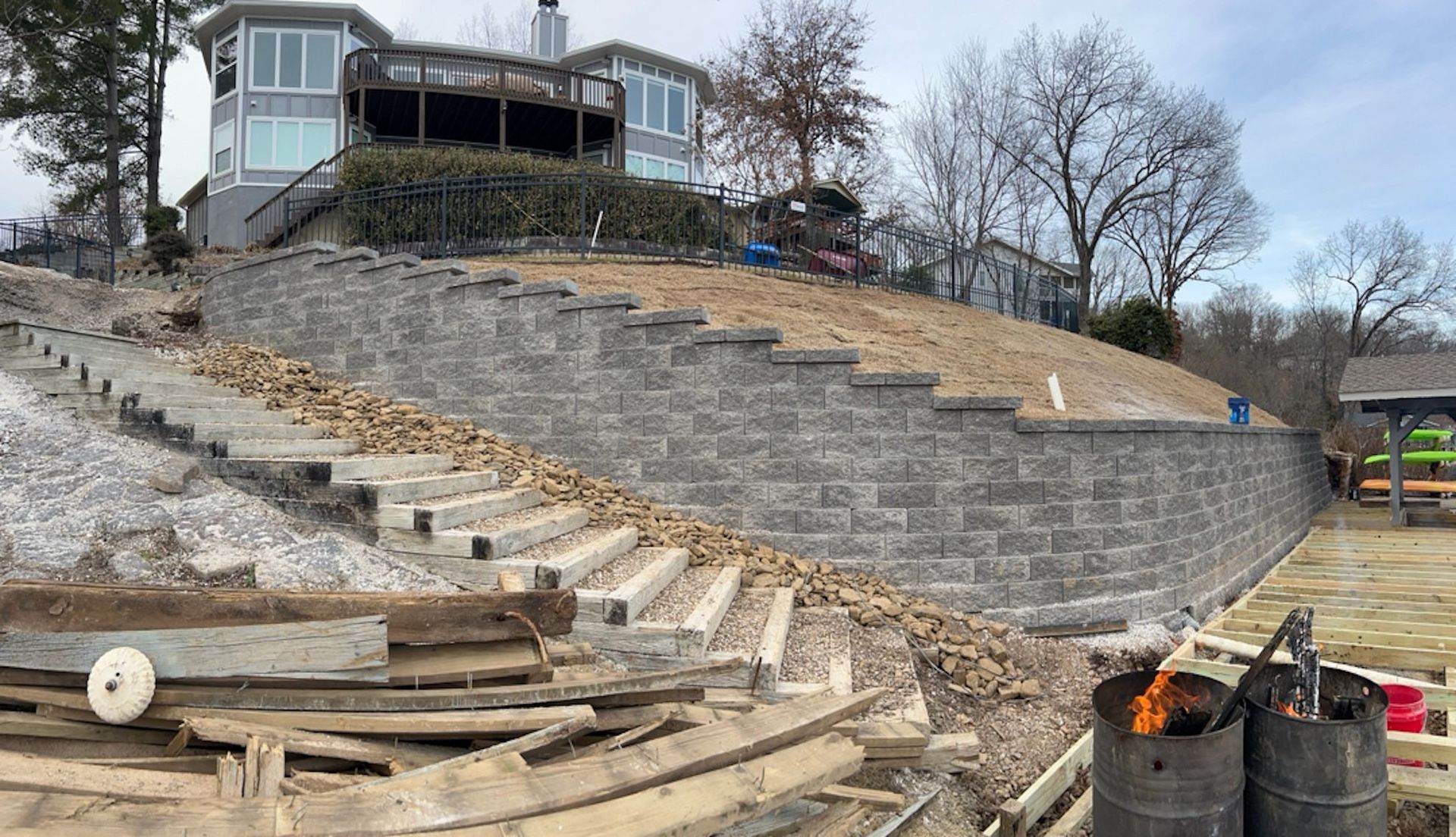 Retaining wall construction with stairs leading up a hillside to a house, with construction debris in foreground.