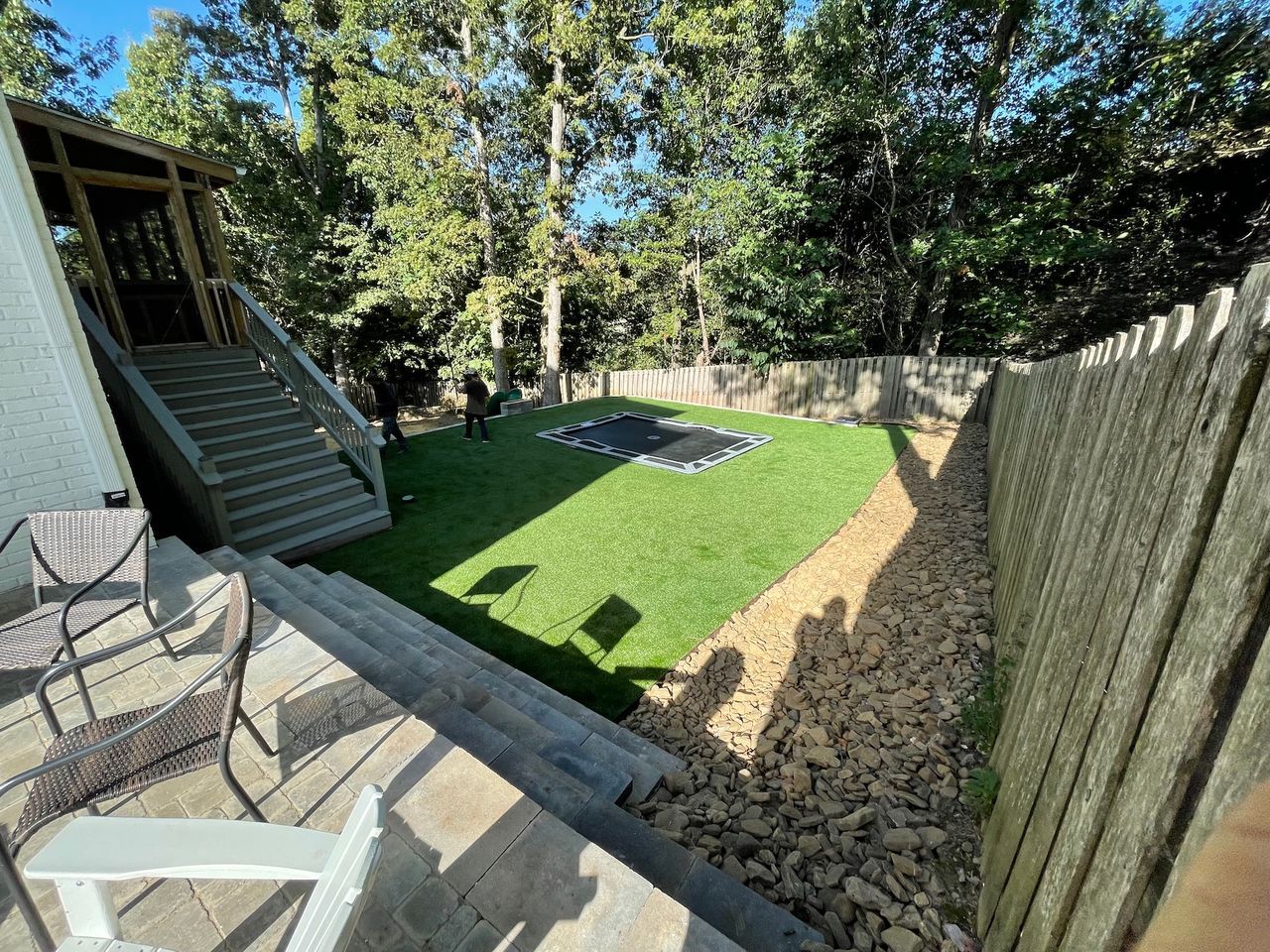 Backyard with steps, green turf, fire pit, gravel path, and wooden fence.