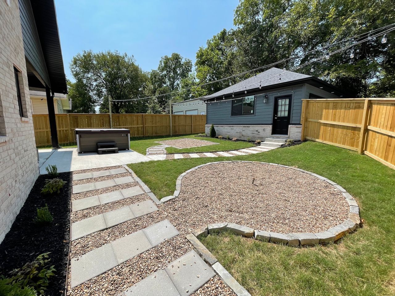Backyard with hot tub, gravel patio, stepping stone pathway, small building, and wooden fence.