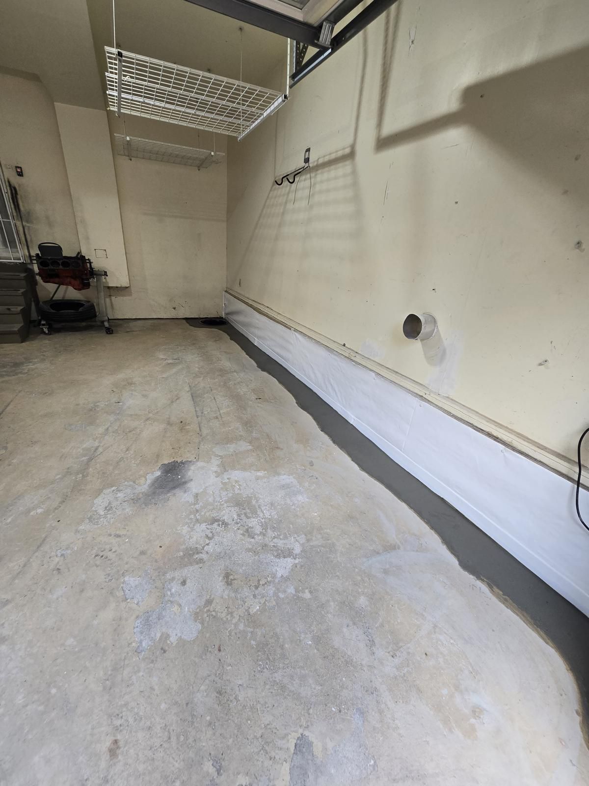 Empty garage with concrete floor, white walls, and a ceiling storage rack.