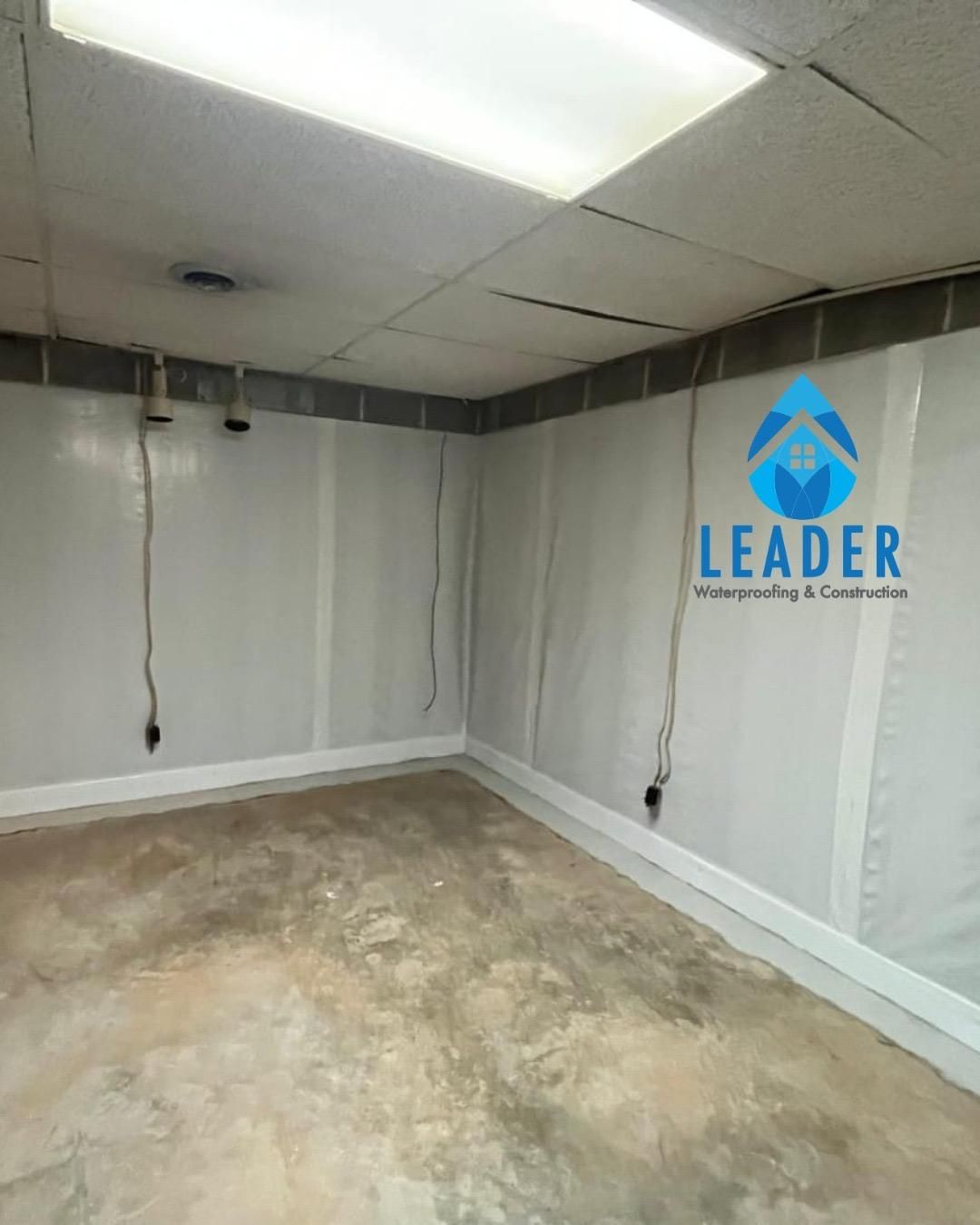 Empty room with gray walls, concrete floor, ceiling lights, and a blue LEADER logo on the wall