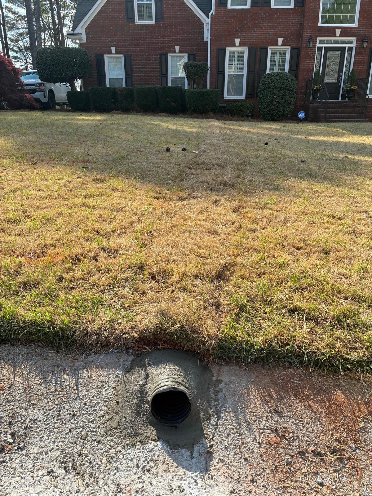 Front yard with a drainage pipe opening at the curb in front of a brick house.