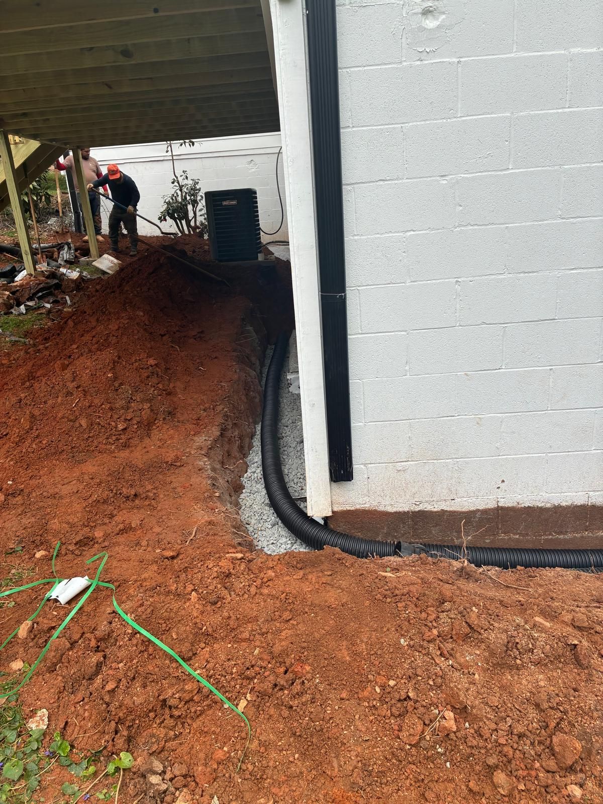 Construction worker on a dirt path beside a white building, under an overhang with exposed pipes.