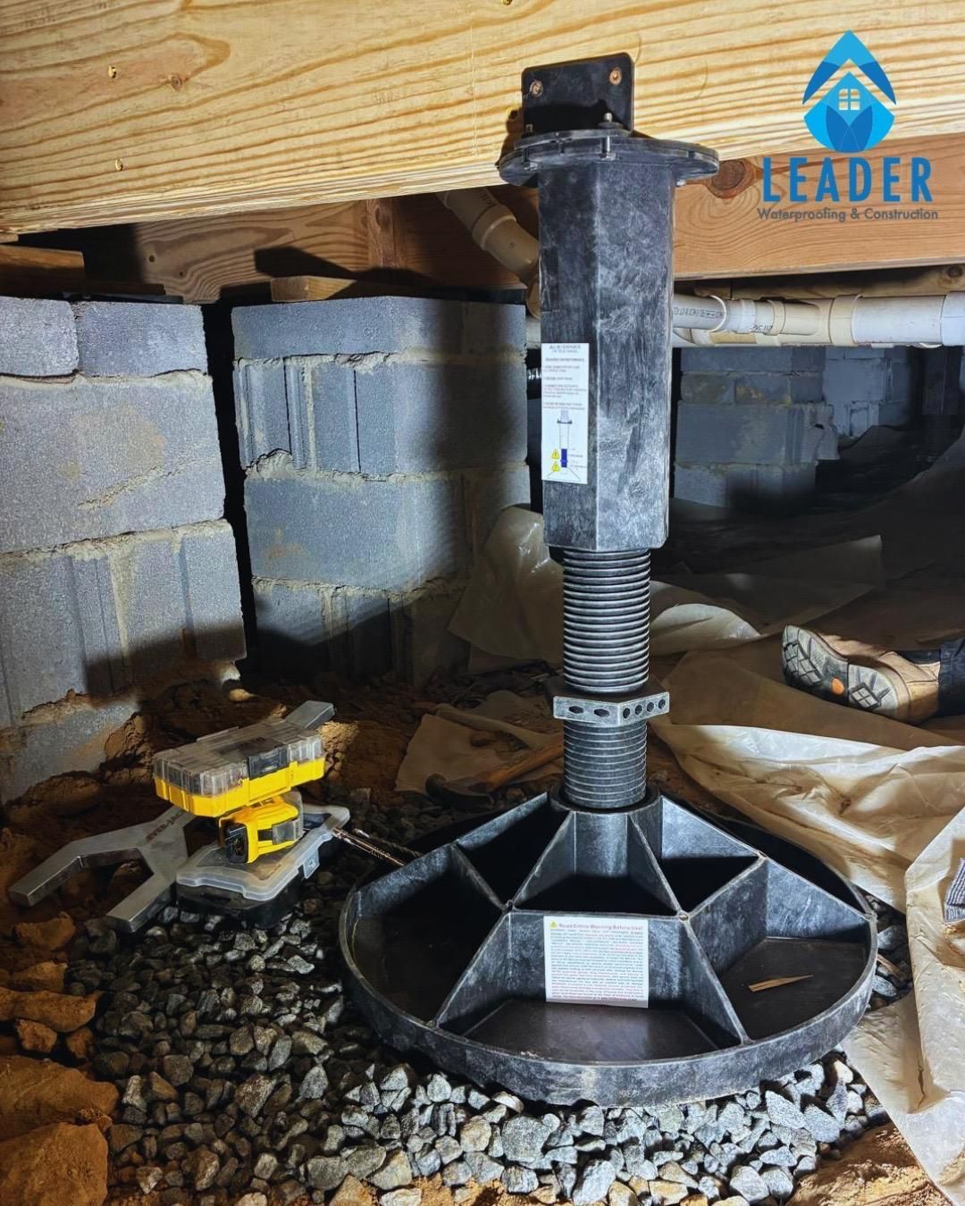 Crawlspace jack post on gravel under floor joists, with cinder blocks and tools nearby.