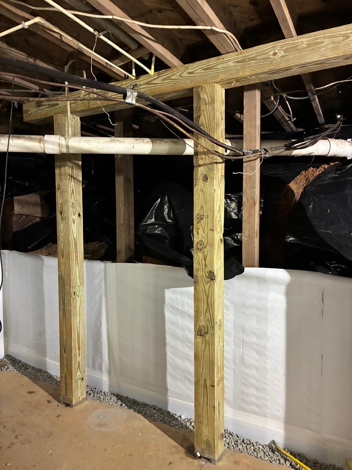 Unfinished attic with wooden beams, white insulation foam walls, and exposed black plastic sheeting.