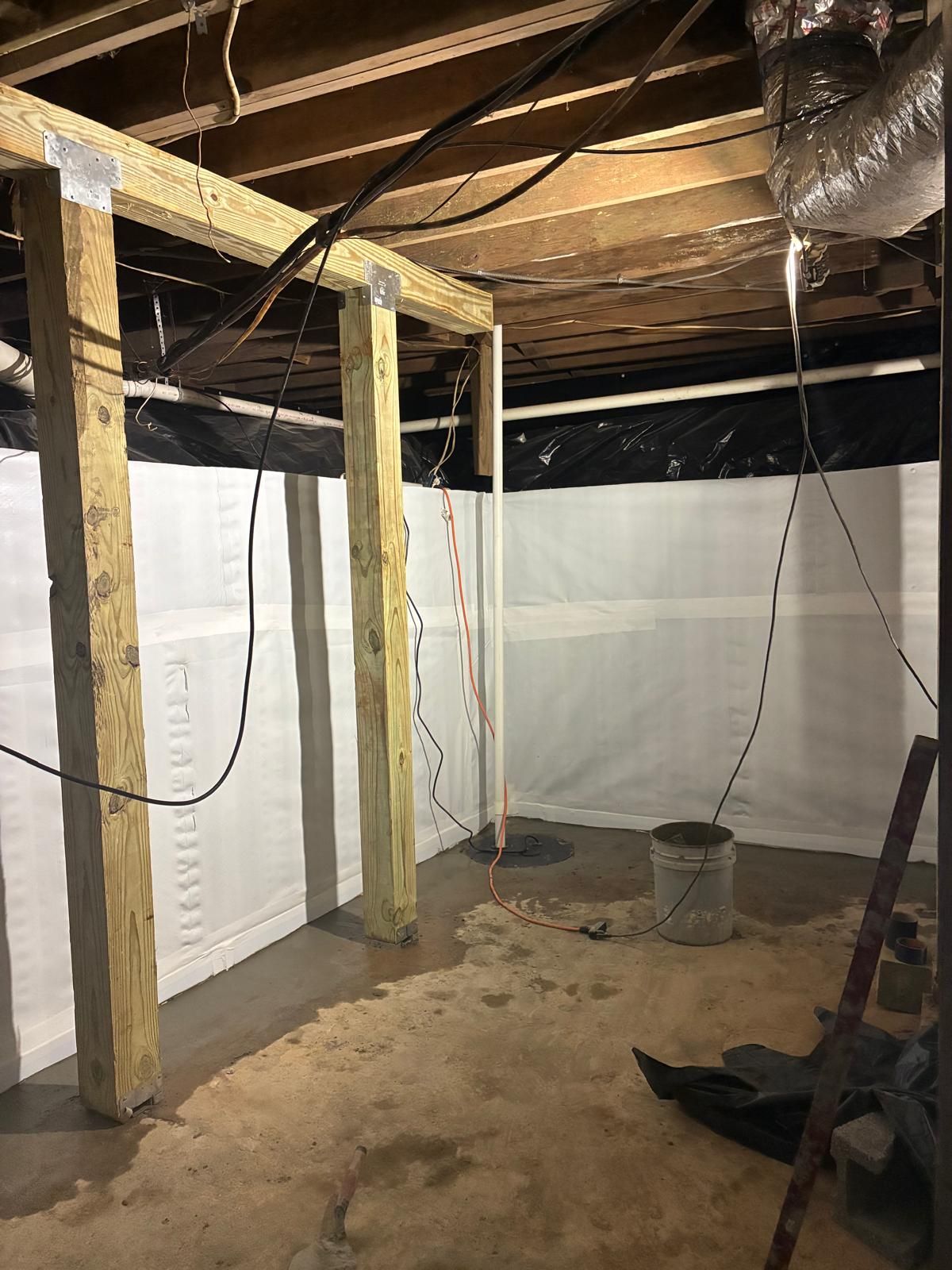 Unfinished basement with exposed ceiling joists, insulation, hanging wires, and a dirt floor.