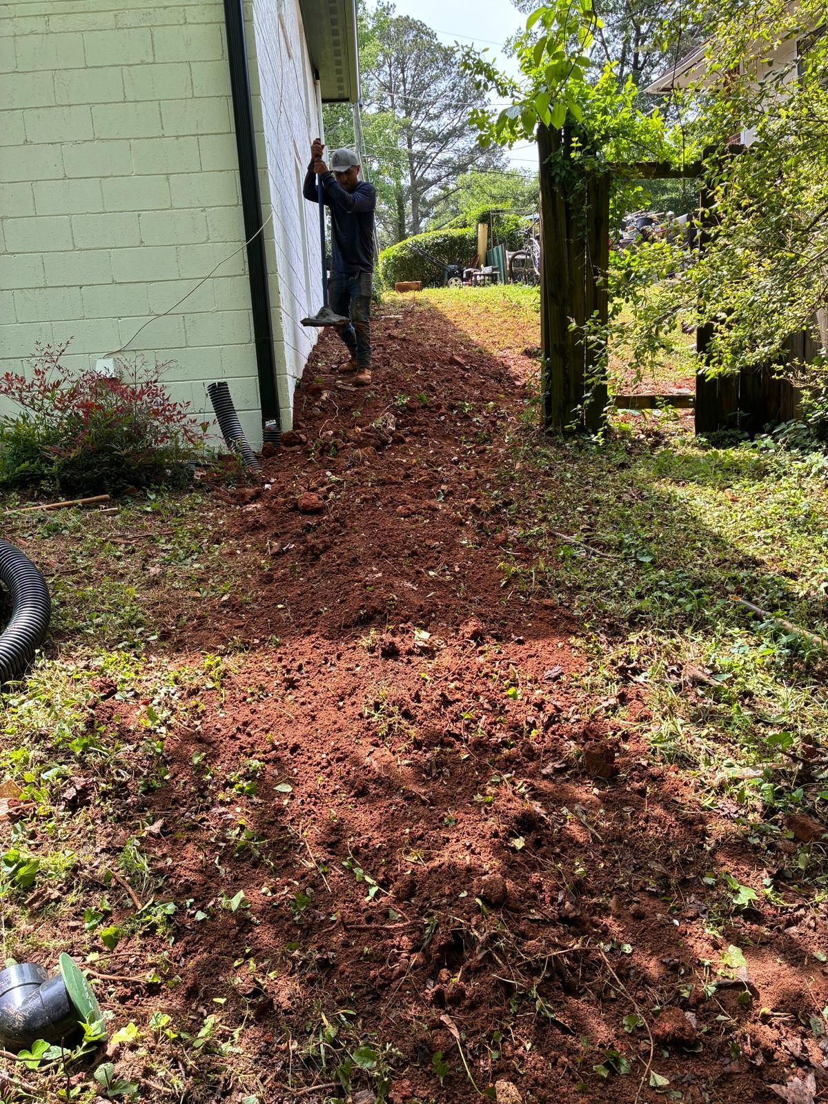 Person standing beside a house on a sloped dirt path in a wooded yard