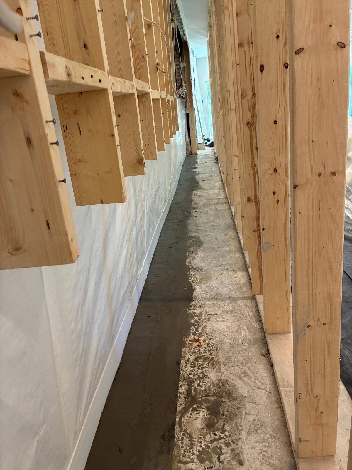 Narrow side passage between wooden wall framing and a white-covered wall, with a concrete floor.