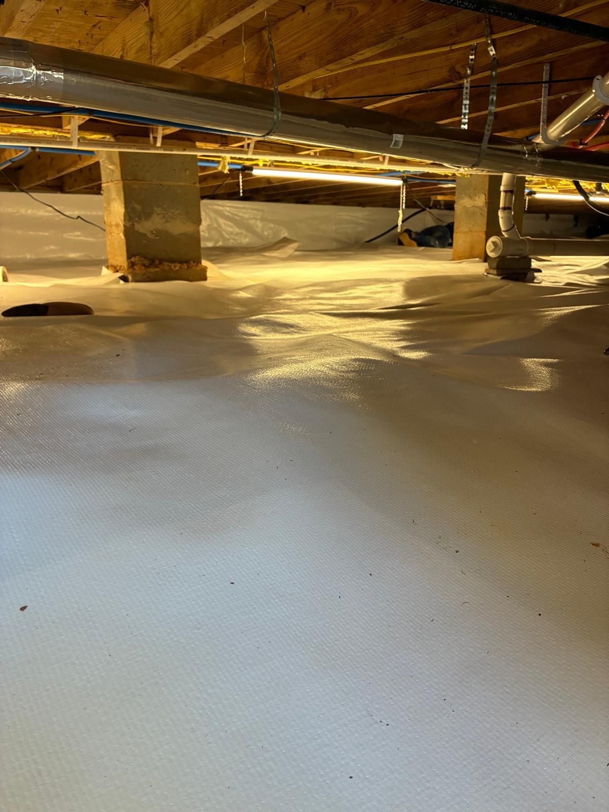 Insulated crawl space with exposed beams, pipes, and ducts under a wooden floor