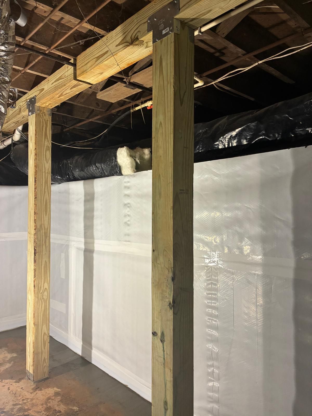 Exposed basement framing with wooden posts, white insulated wall panels, and open ceiling joists.