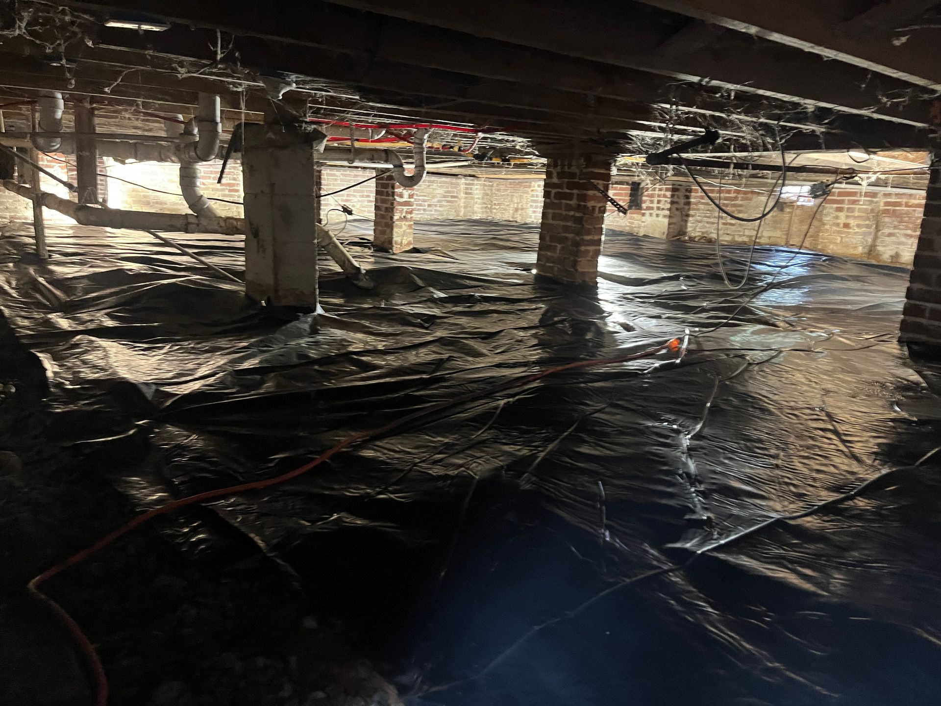 Flooded basement with standing water, support columns, and plastic sheeting on the floor