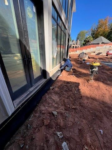 Worker installing exterior siding beside a modern building on a muddy construction site.