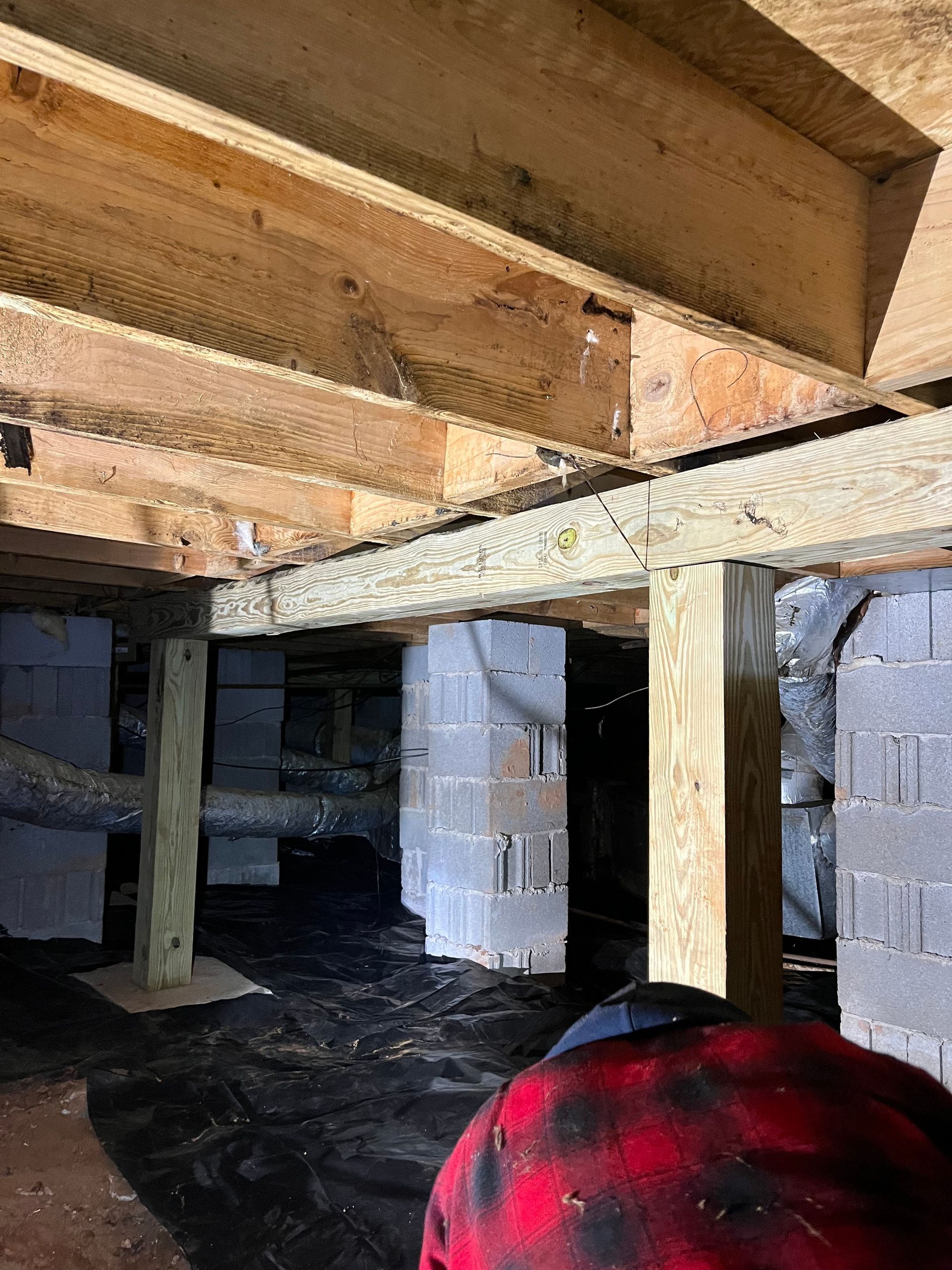 Cinder block crawlspace under wooden beams, with a red-and-black plaid hat in the foreground
