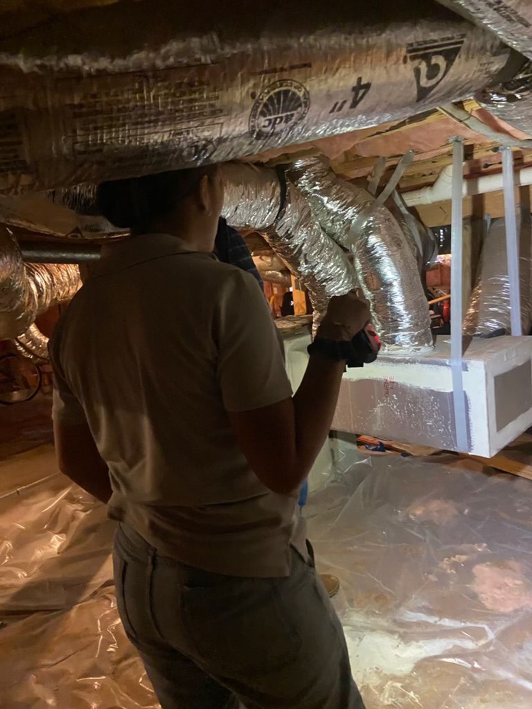 Person inspecting shiny insulated ductwork in an attic crawlspace