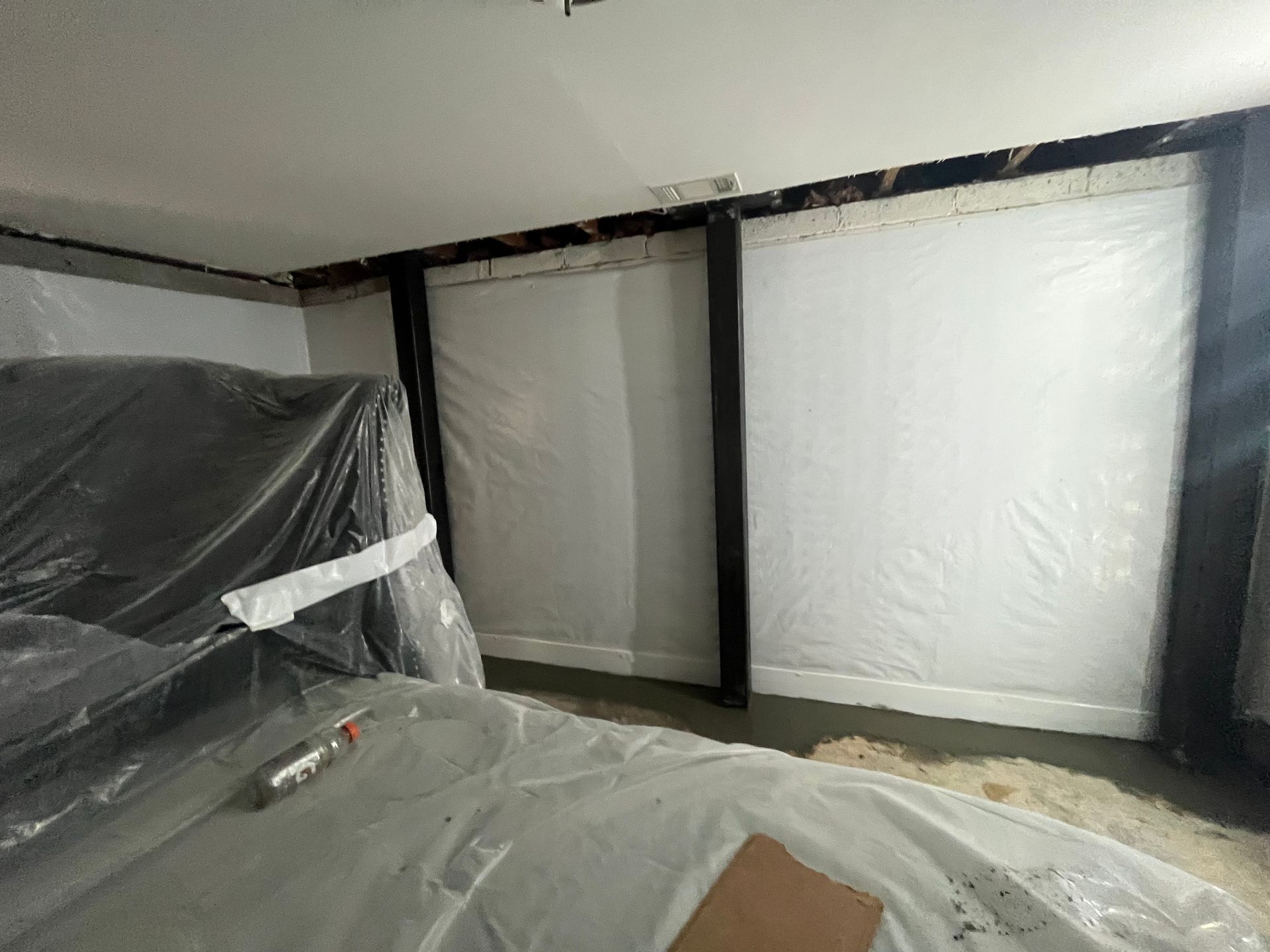 Room under renovation with plastic-covered furniture and white insulated walls