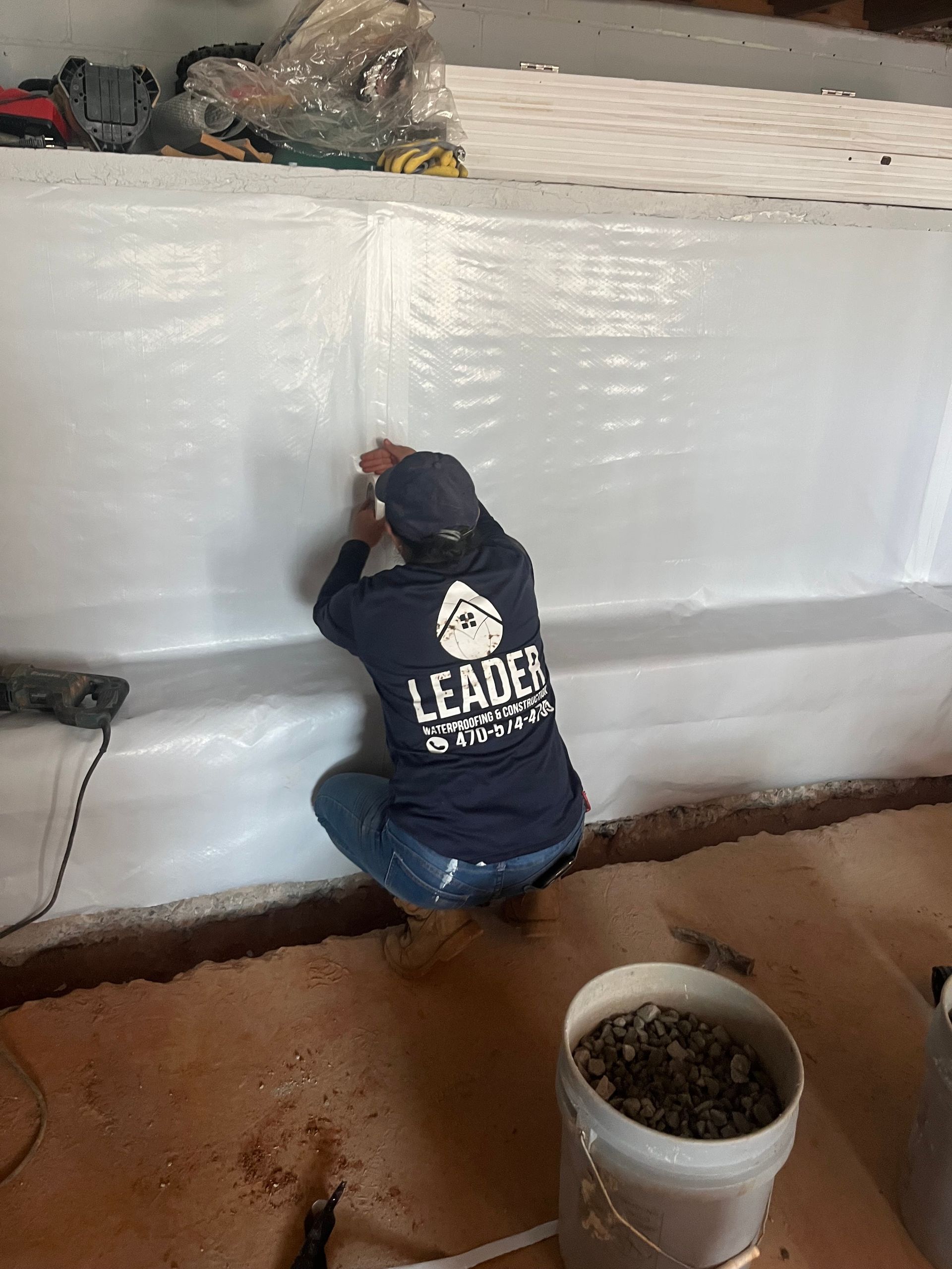 Person crouches indoors, applying sealant to a white wall beside an insulation-lined opening.