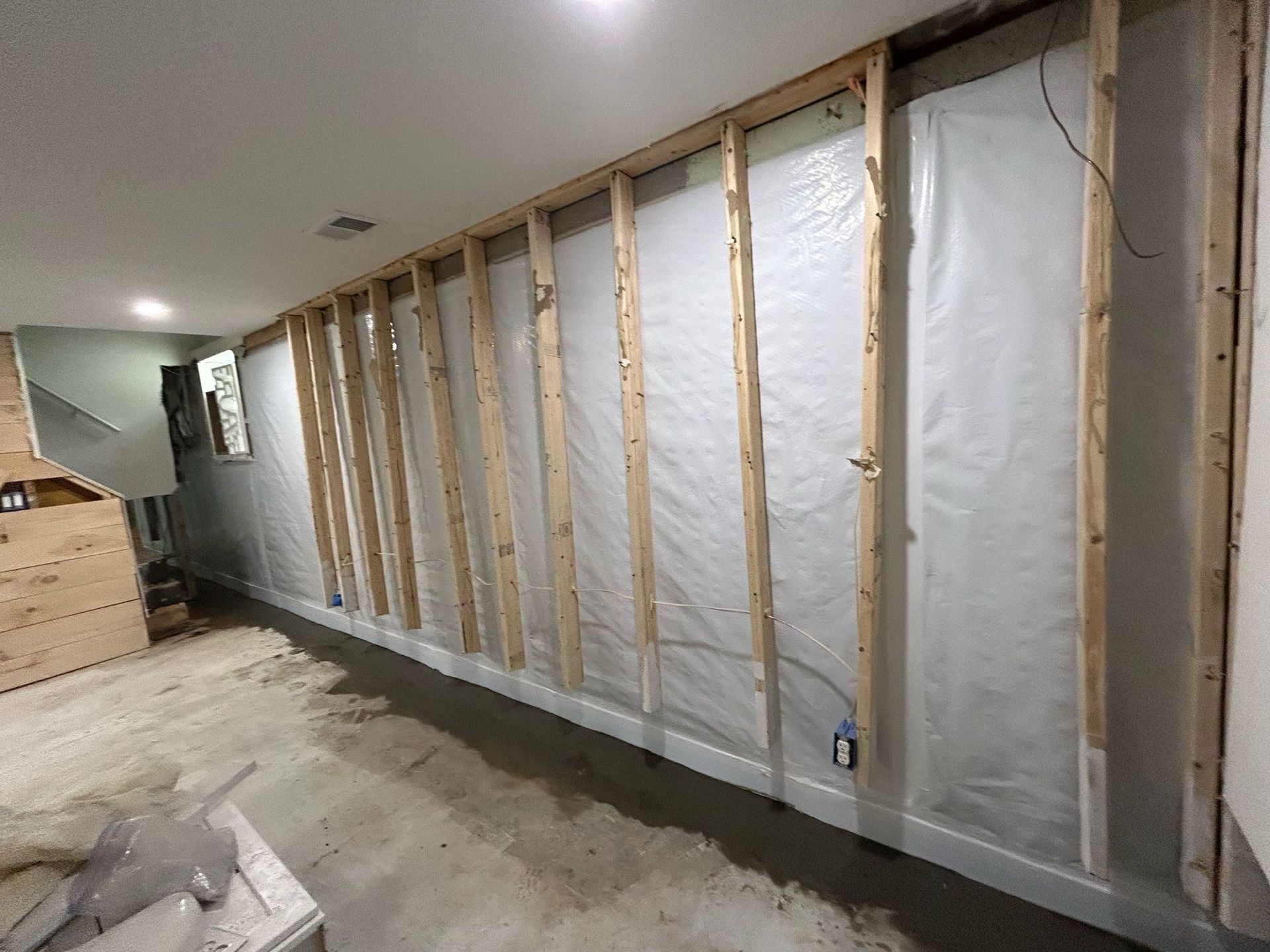 Unfinished basement wall with exposed wooden studs and white insulation panels along a concrete floor.