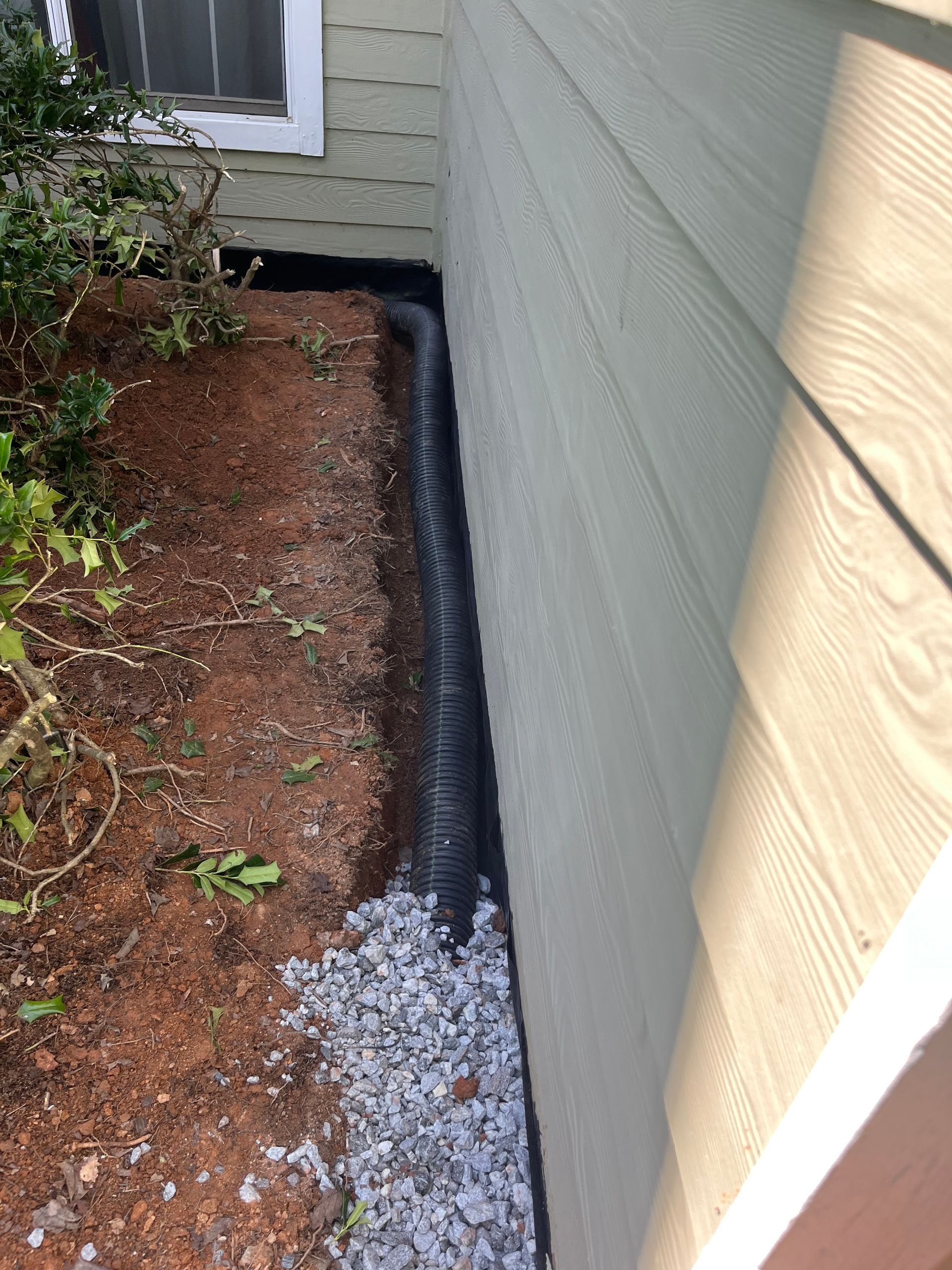 Narrow side yard with mulch bed and white gravel drainage strip beside a house wall.