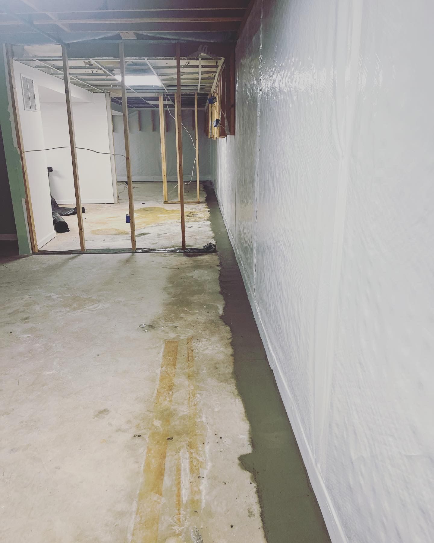 Narrow unfinished hallway with plastic-covered wall, exposed framing, and stained concrete floor.