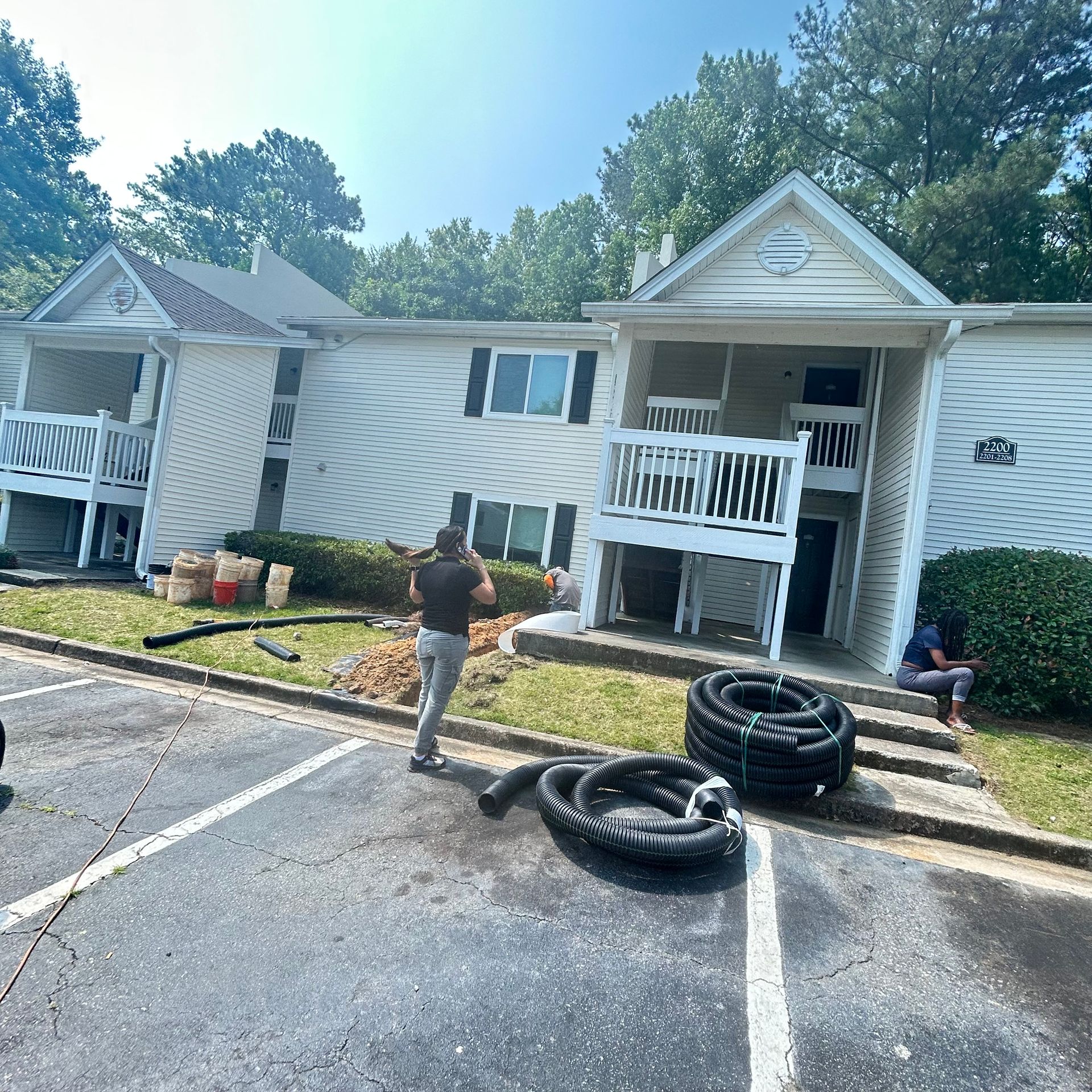 Apartment building with damaged siding, two people outside, and large tires in the parking lot