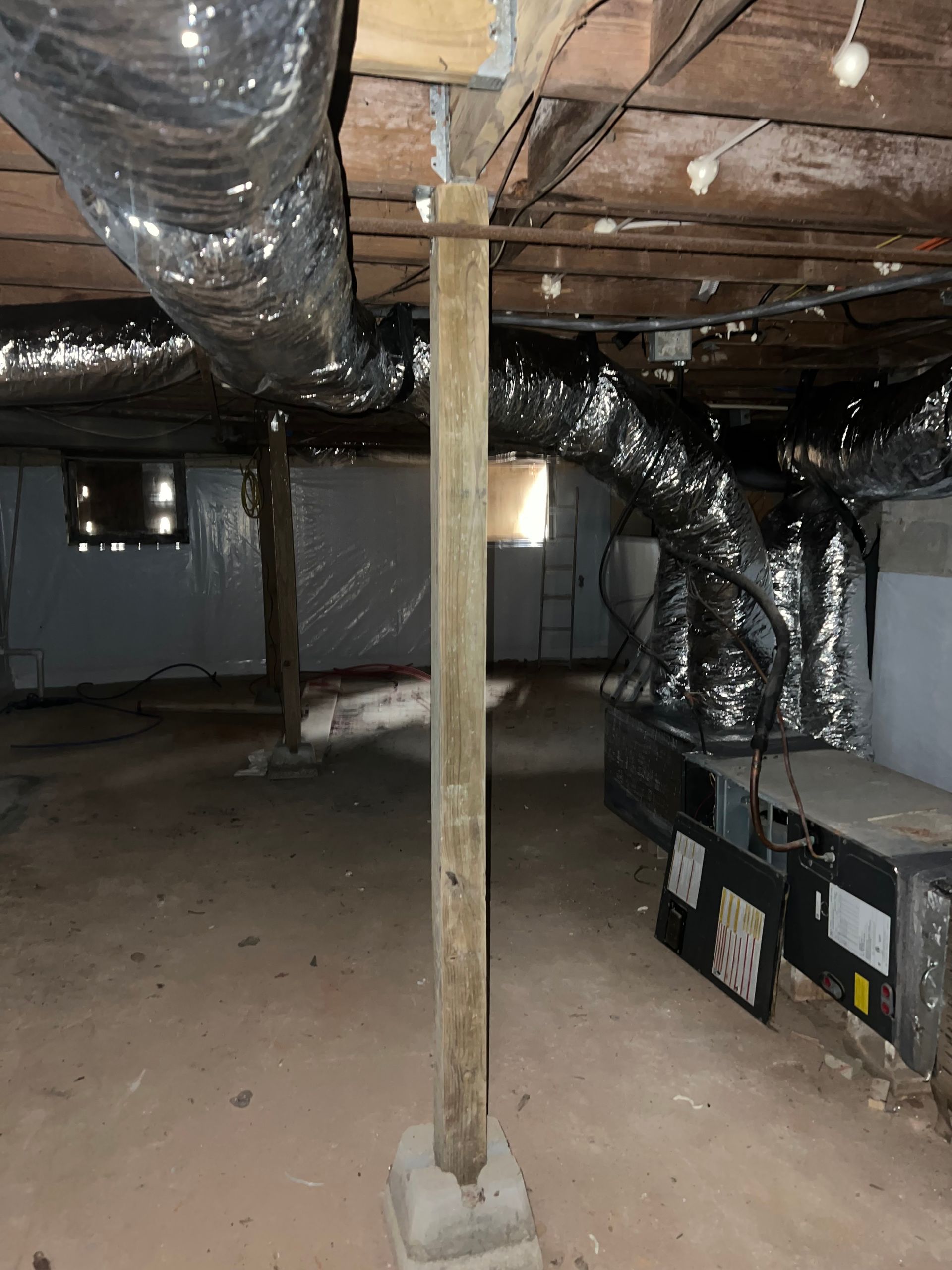Basement crawlspace with exposed beams, ductwork, support post, and HVAC units.