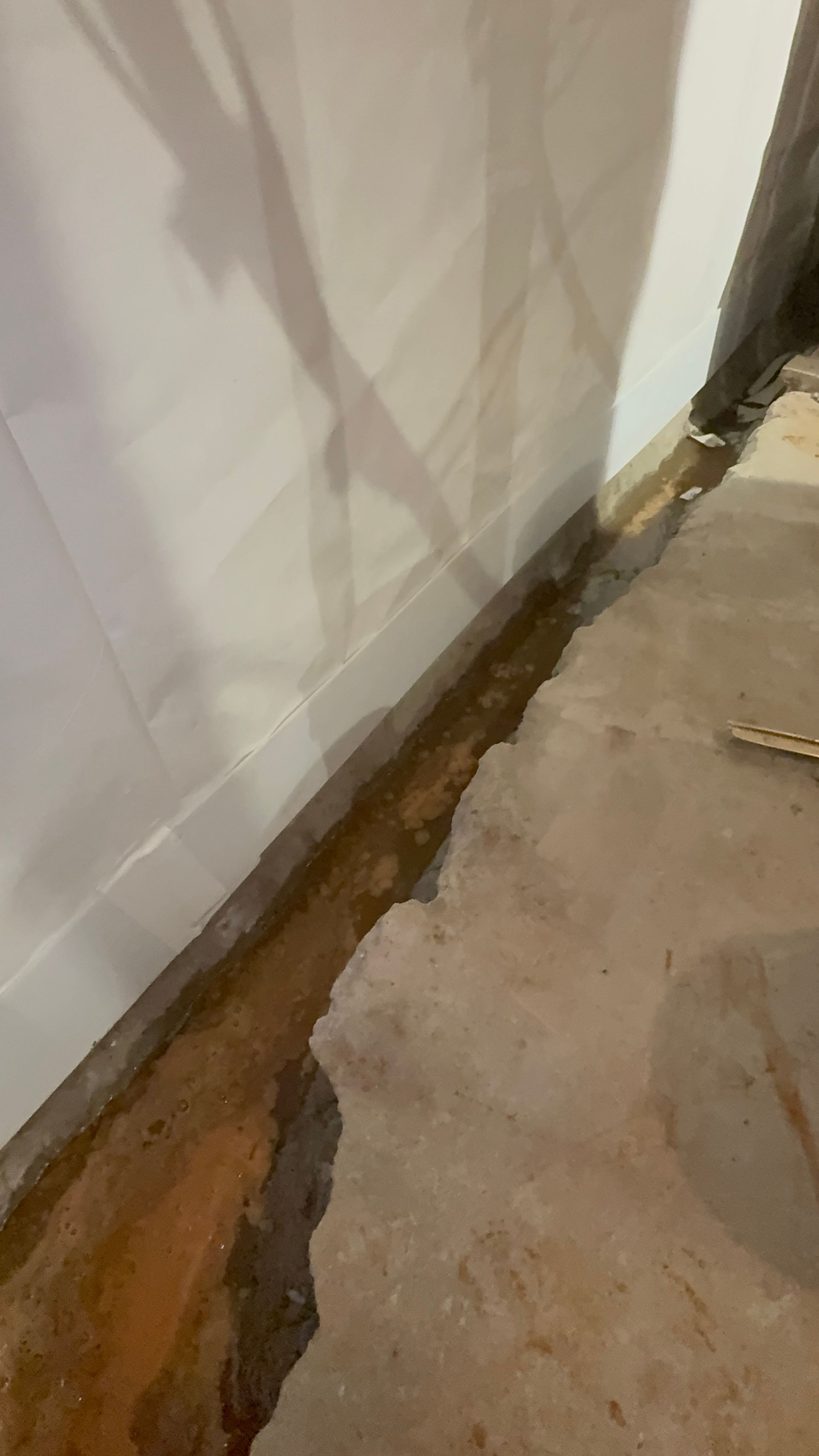 Damaged base of a wall with exposed wood and crumbling plaster along a concrete floor