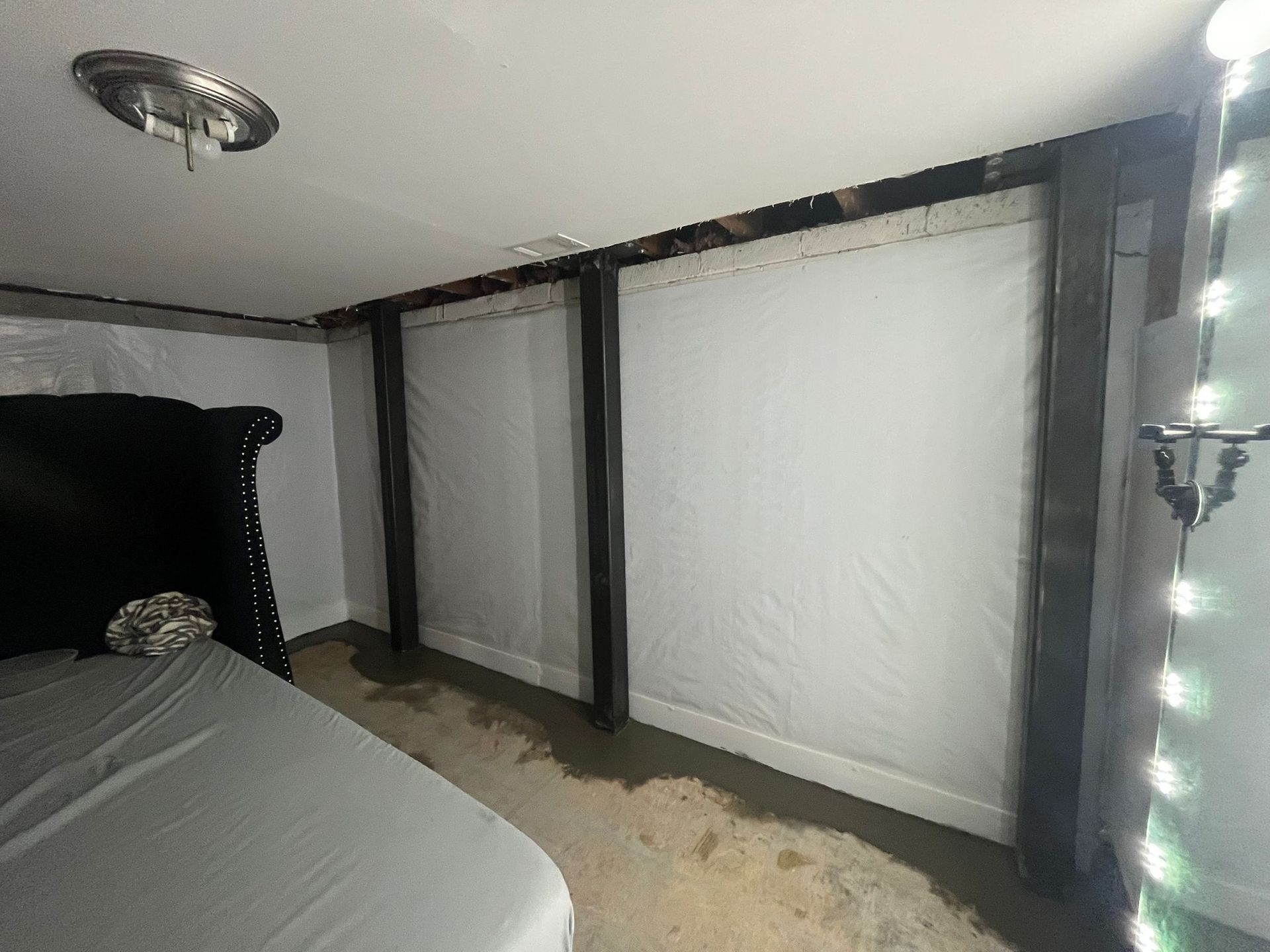 Bedroom with a bed, dark canopy posts, white wall panels, and string lights along the right side.