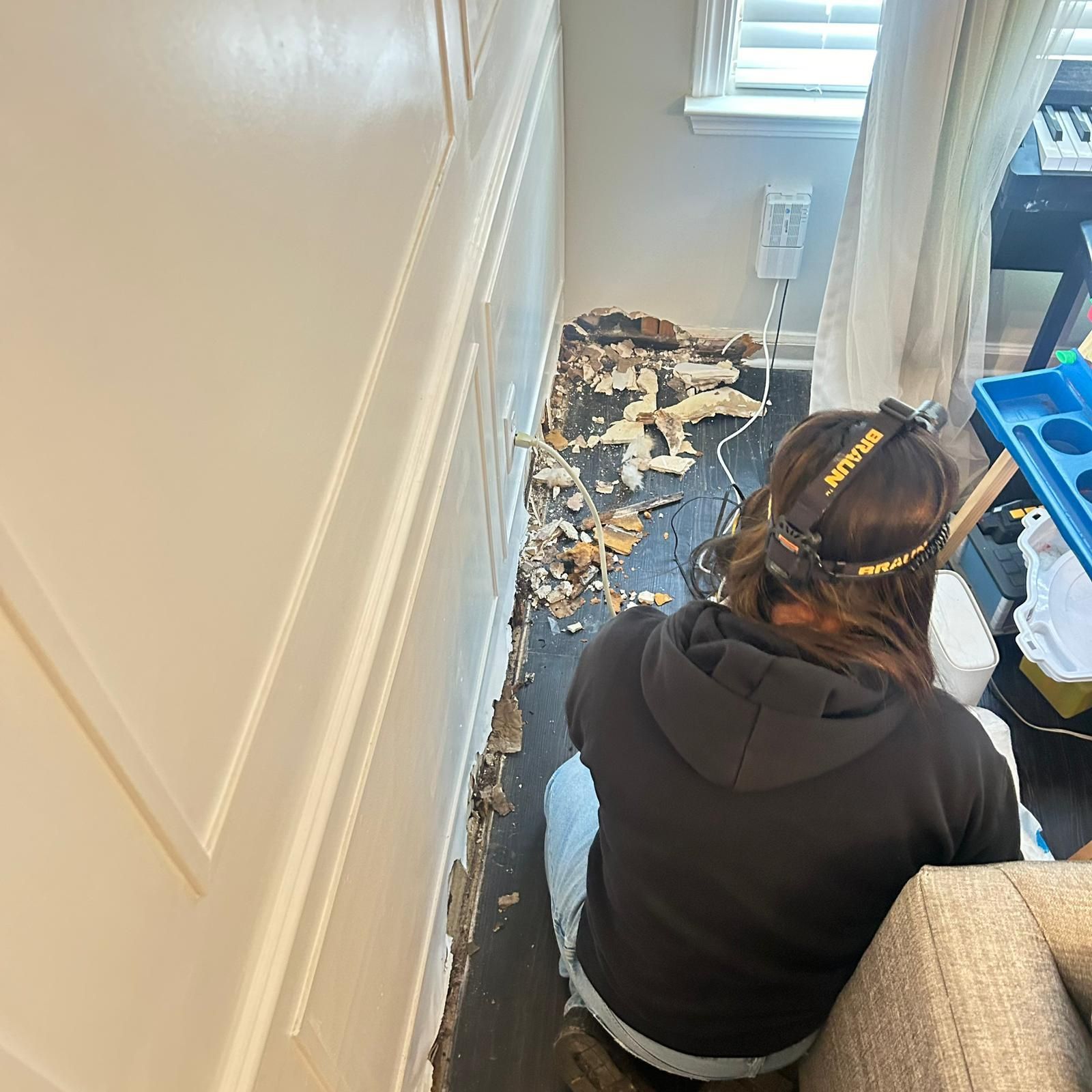 Worker in a hallway removing damaged flooring and debris near a skylight.