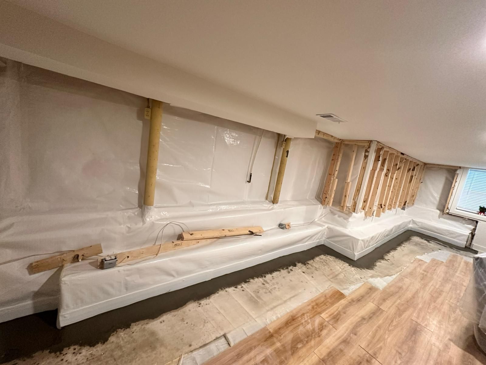 Renovated room with exposed wall framing, plastic sheeting, and hardwood flooring under installation