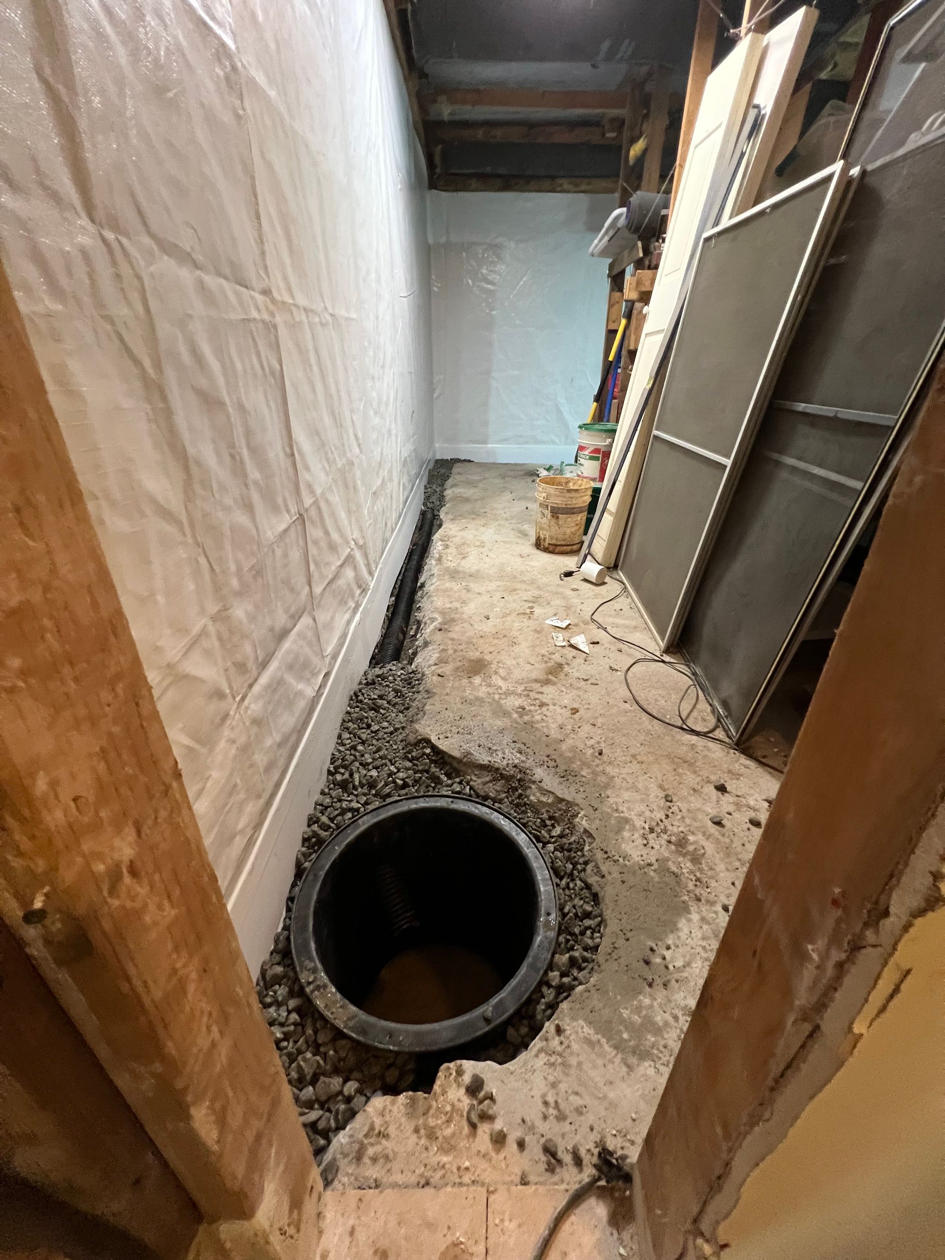 Narrow unfinished basement corridor with a large floor opening and stacked panels on the right