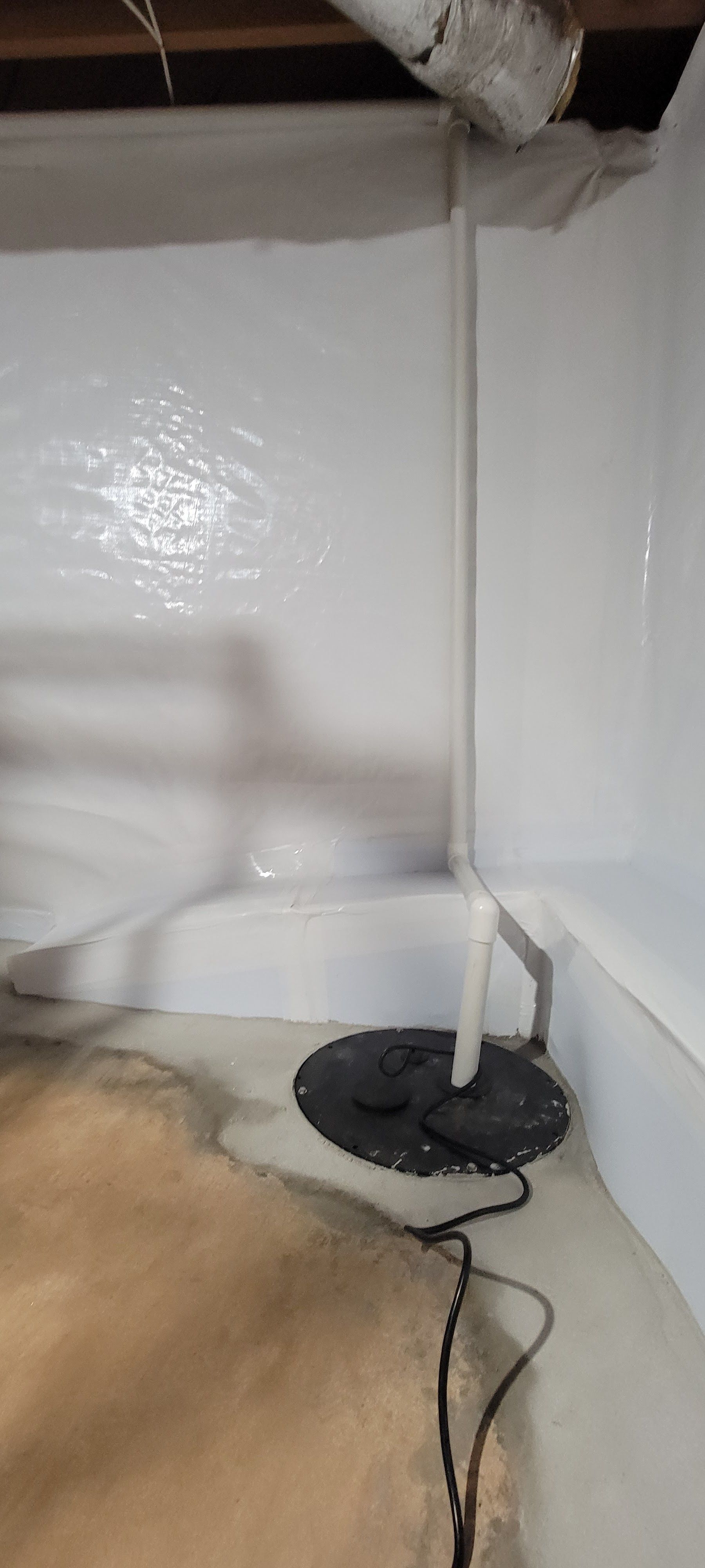 Corner of a room with a white wall, exposed pipe, and a small black-base lamp or stand on the floor
