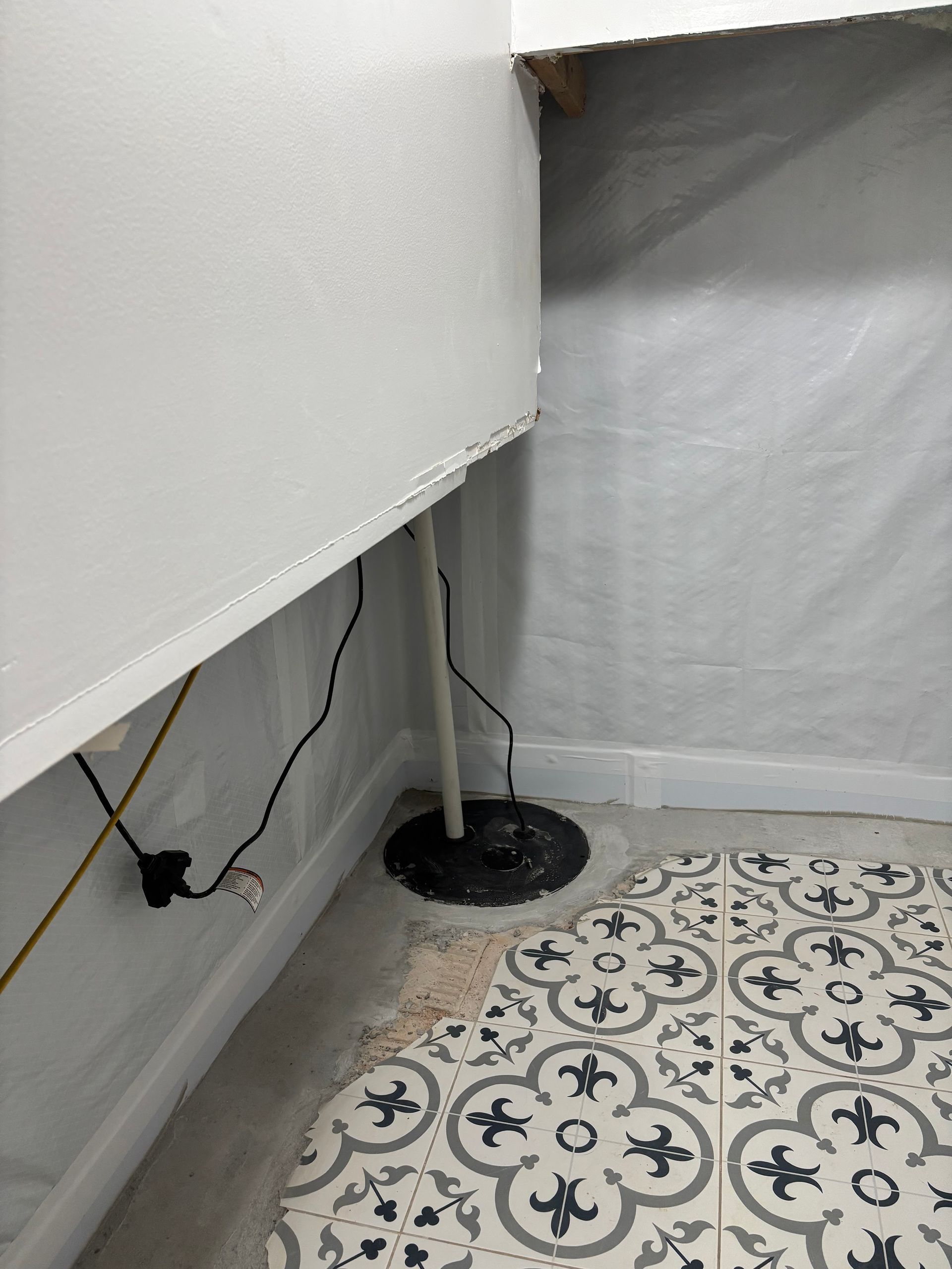 Corner of a room with a white cabinet, visible cables, and a round black base on a patterned floor.