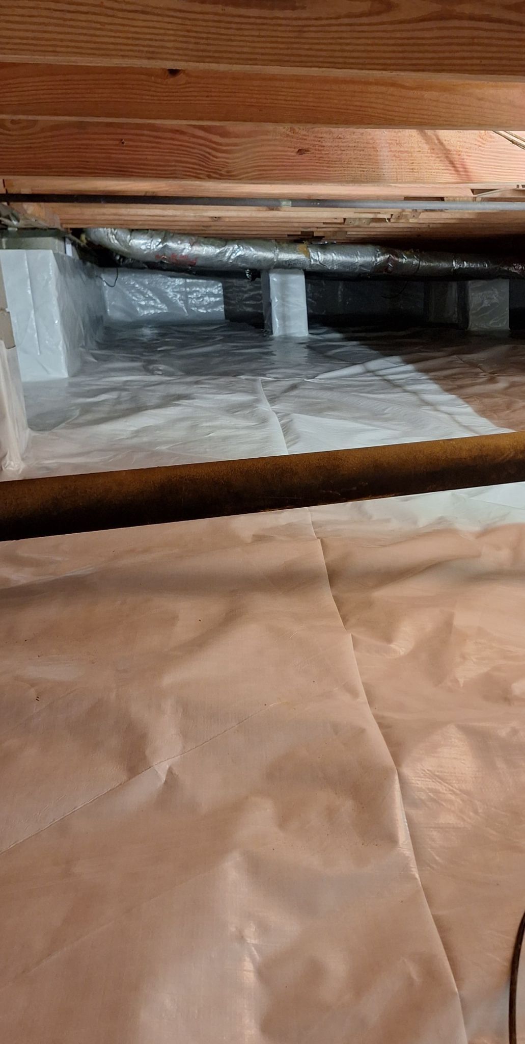 Close-up of a wooden floor gap revealing insulation and a plastic barrier underneath